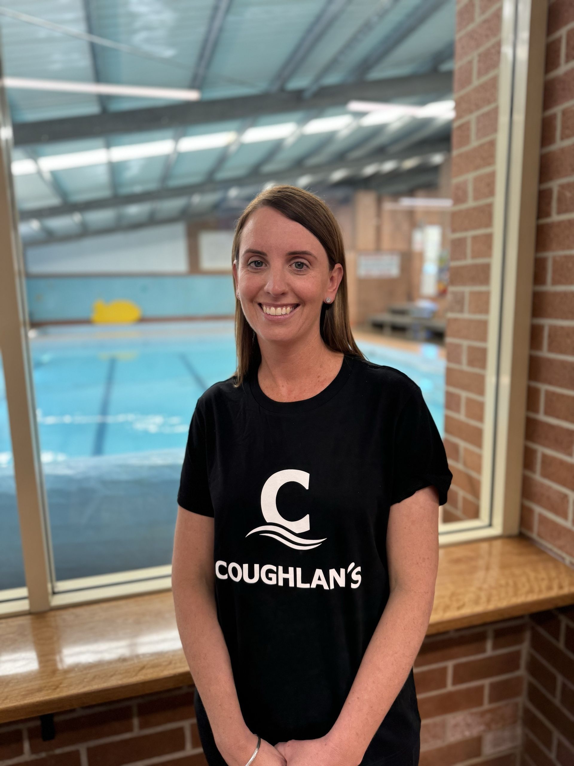 A woman wearing a coughlan 's t-shirt is standing in front of a window.