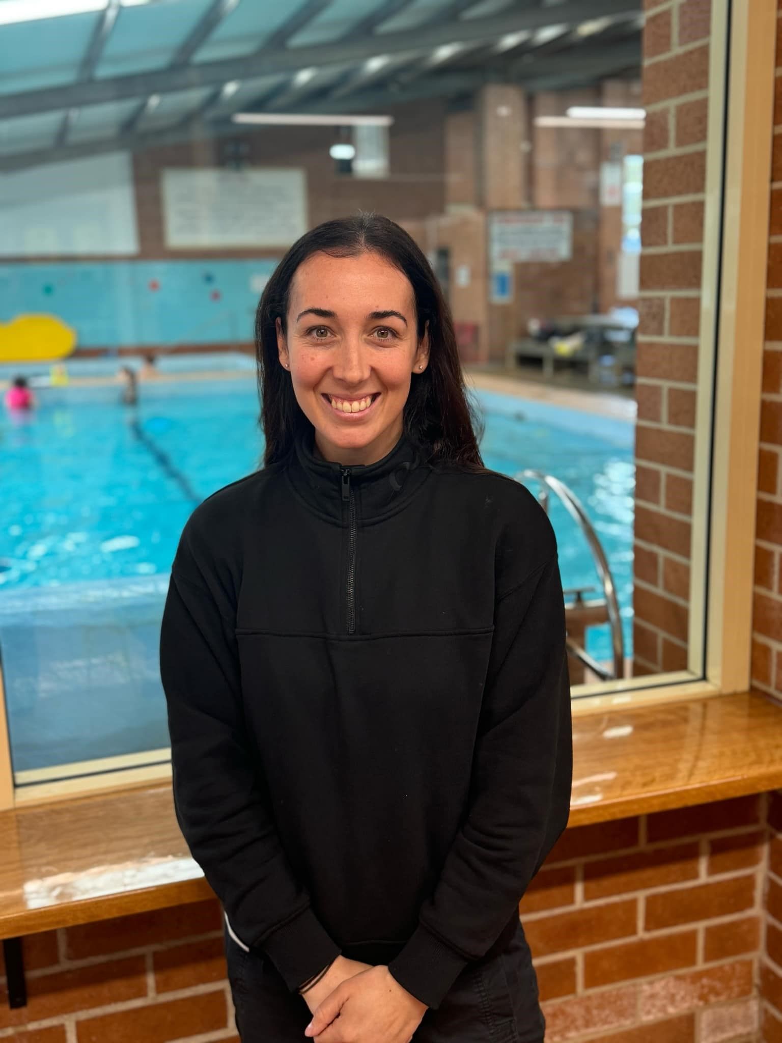 A woman in a black sweater is standing in front of a swimming pool.