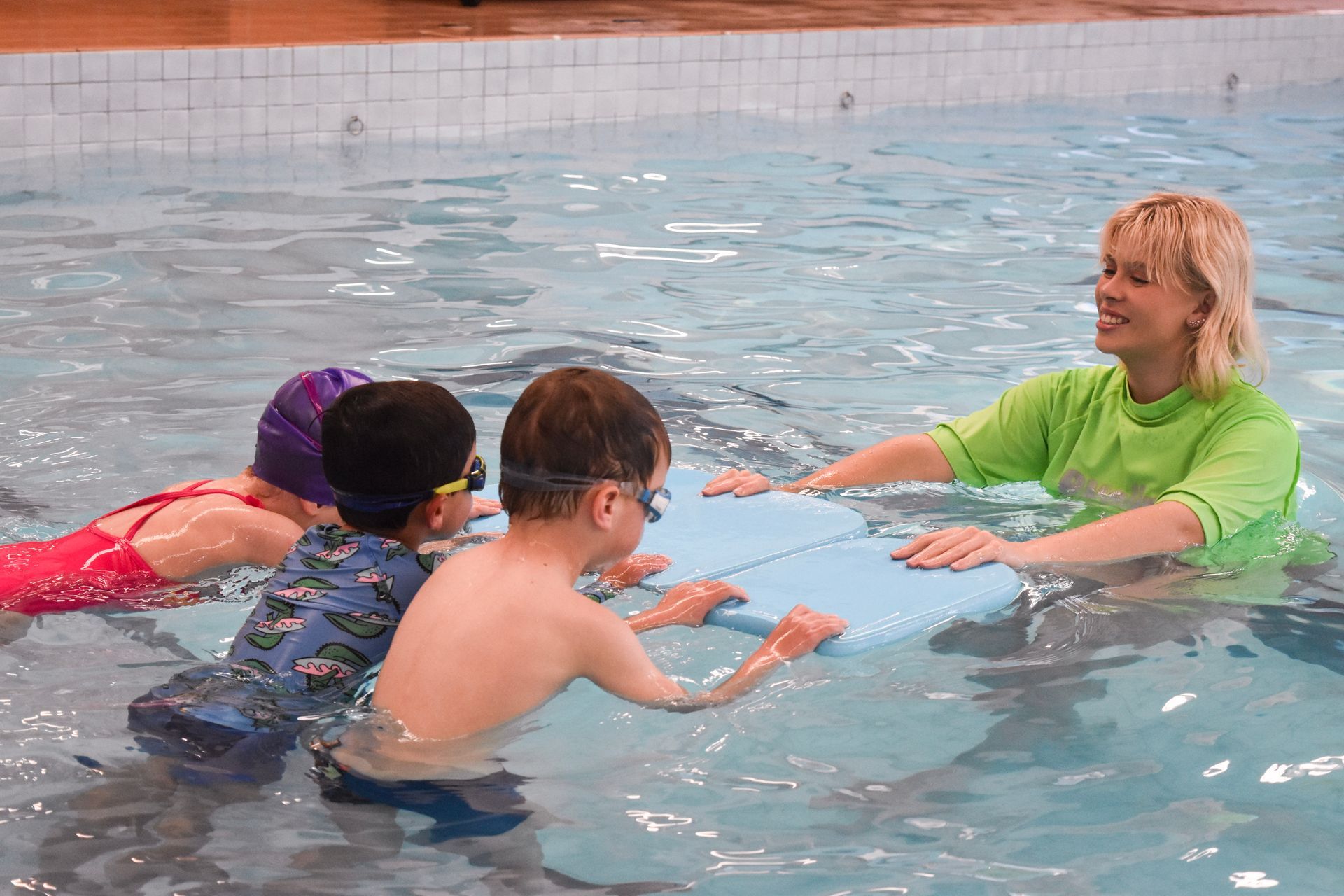 A woman is teaching three children how to swim in a swimming pool.