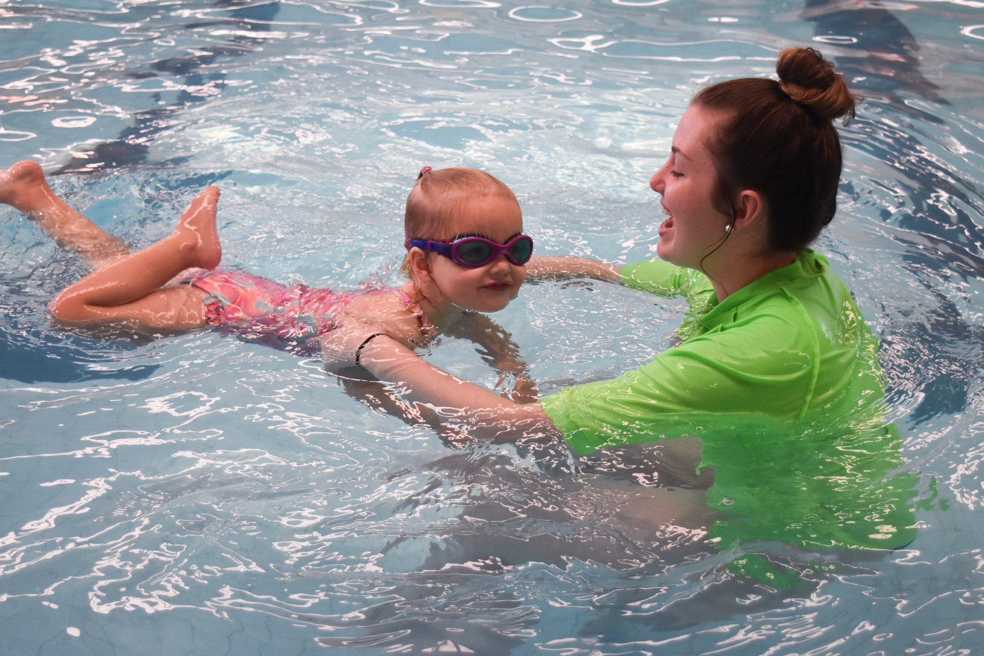 A woman is teaching a little girl how to swim in a swimming pool.