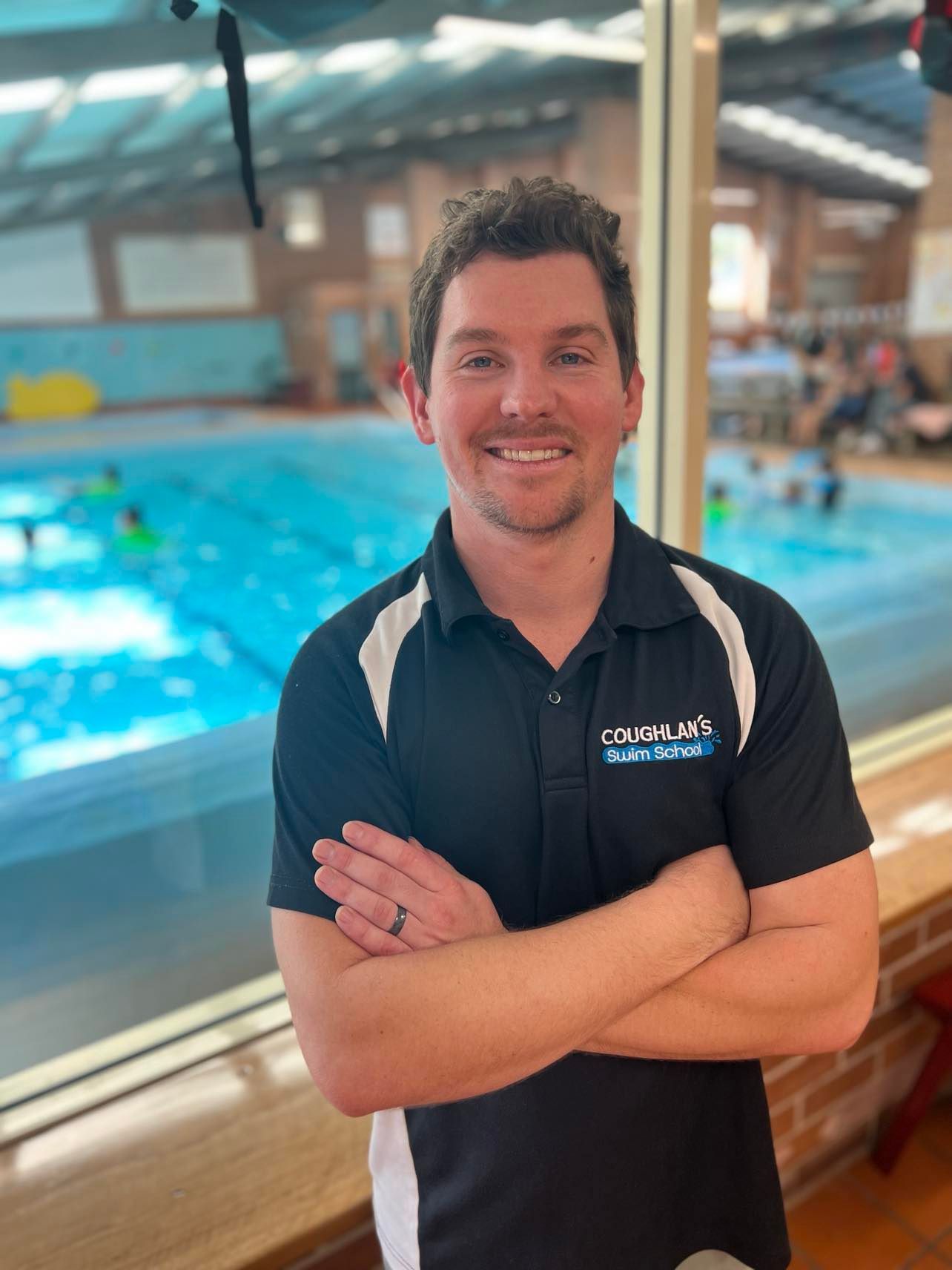 A man is standing in front of a swimming pool with his arms crossed.