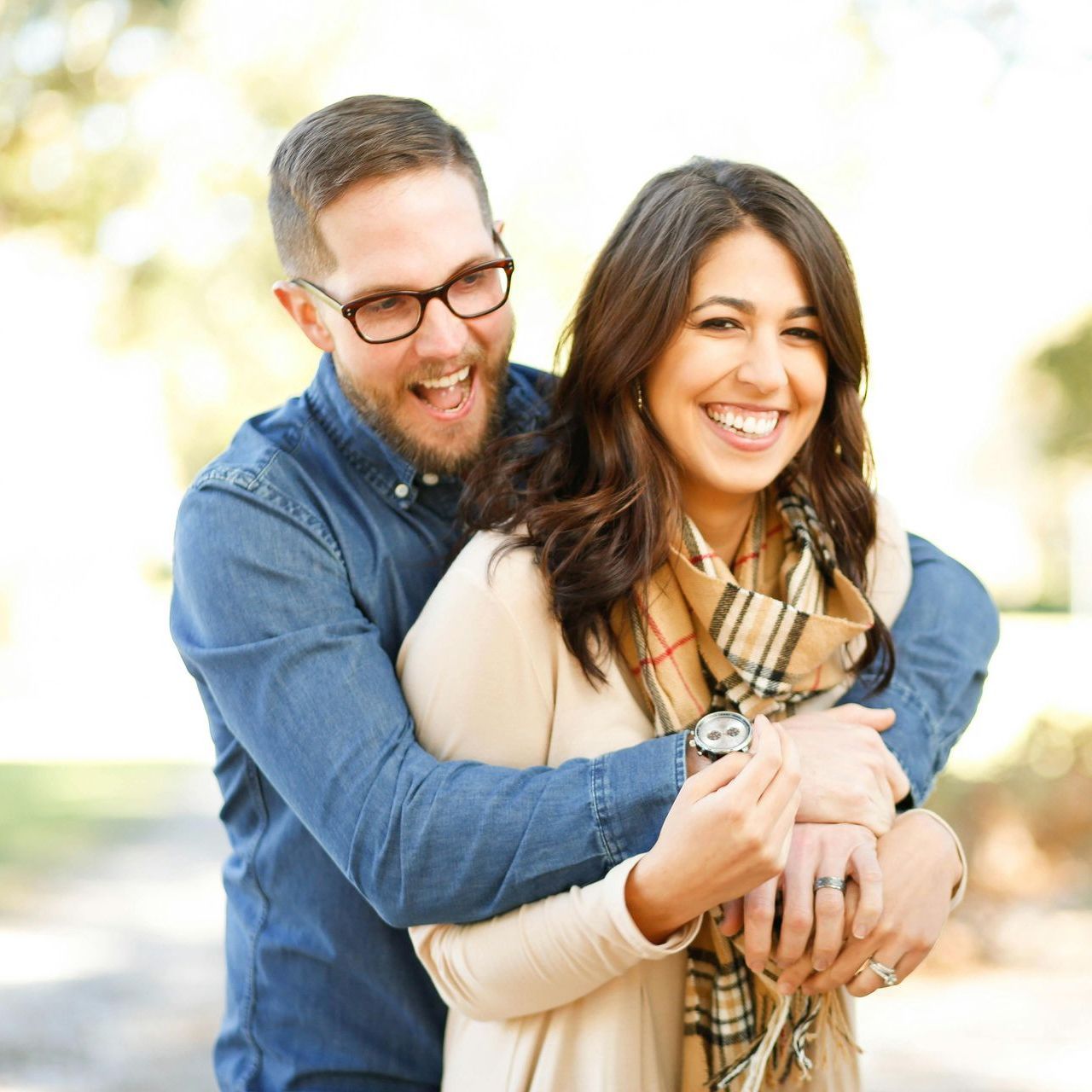 A man in glasses is hugging a woman in a plaid scarf