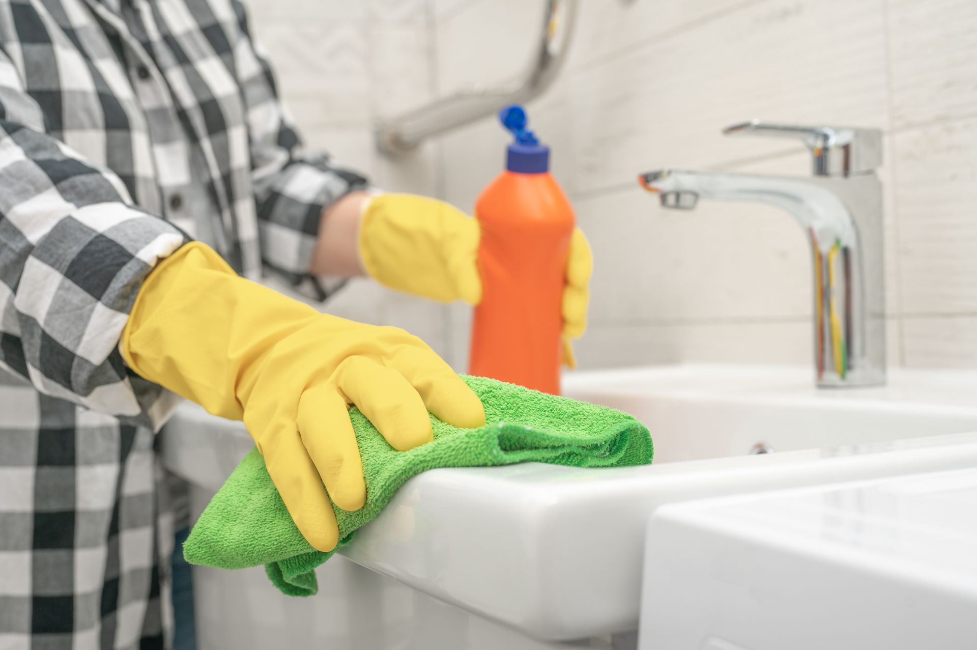 A person wearing yellow gloves is cleaning a sink in a bathroom.