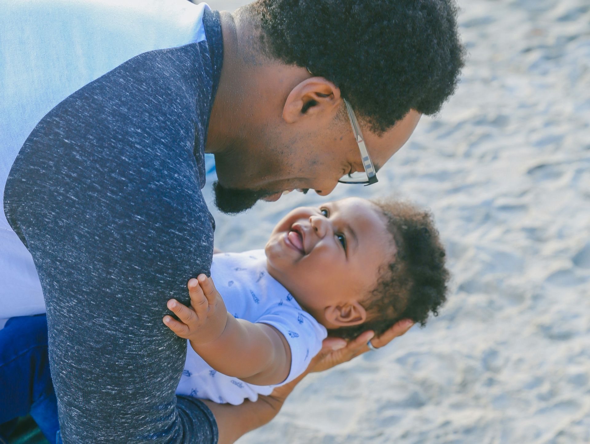 Photo of African American father and son smiling and playing on the beach.
