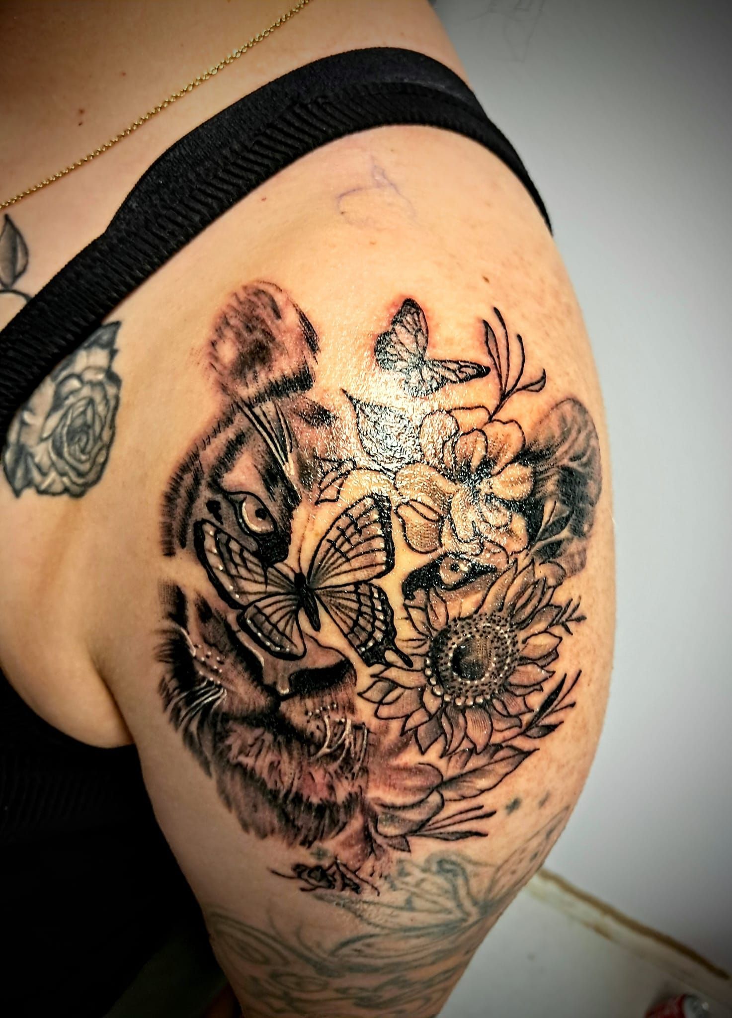 Tattoo of a lion's face and sunflowers on a shoulder, black ink.