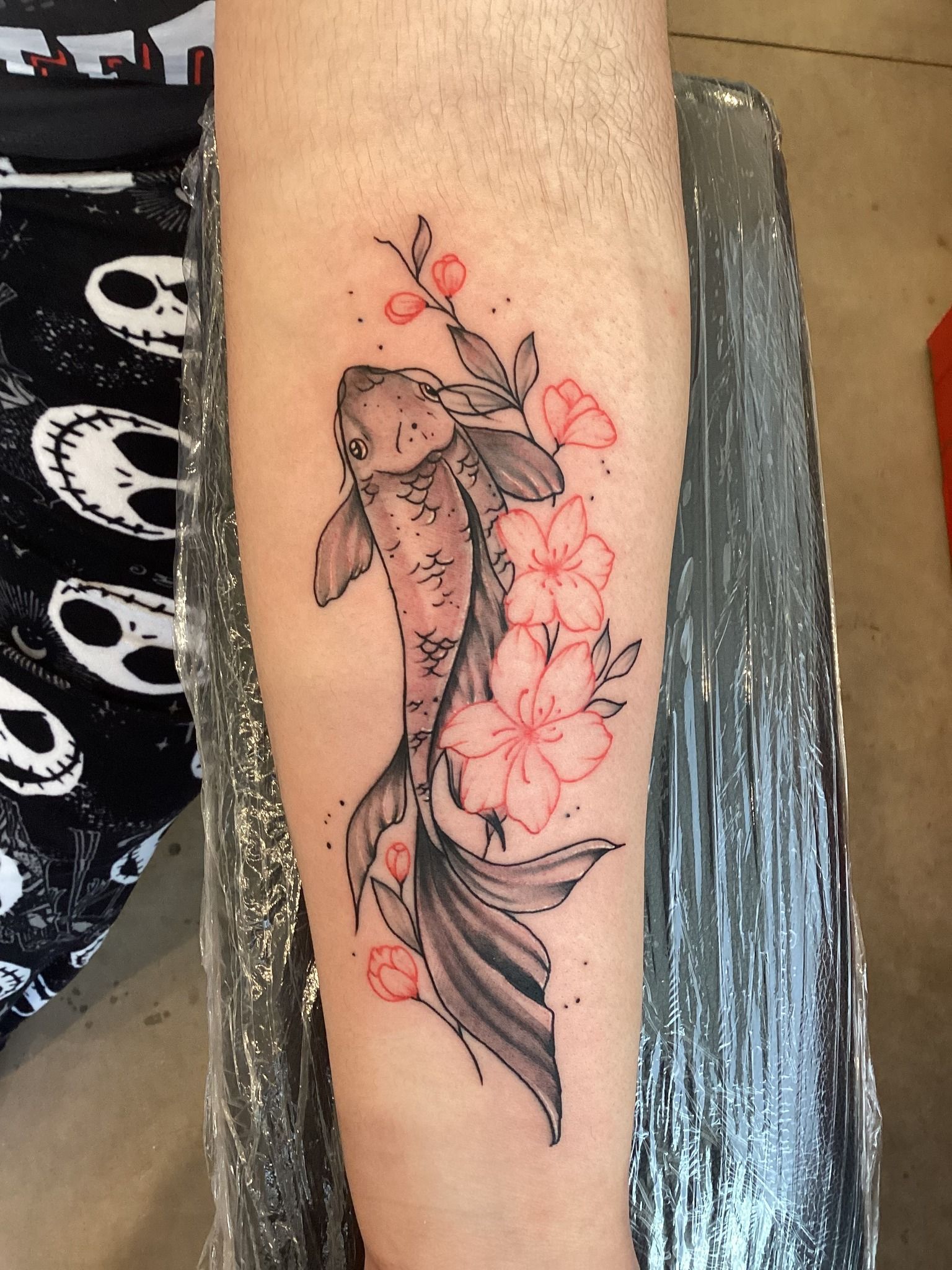 Tattoo of a koi fish and pink cherry blossoms on a person's arm.