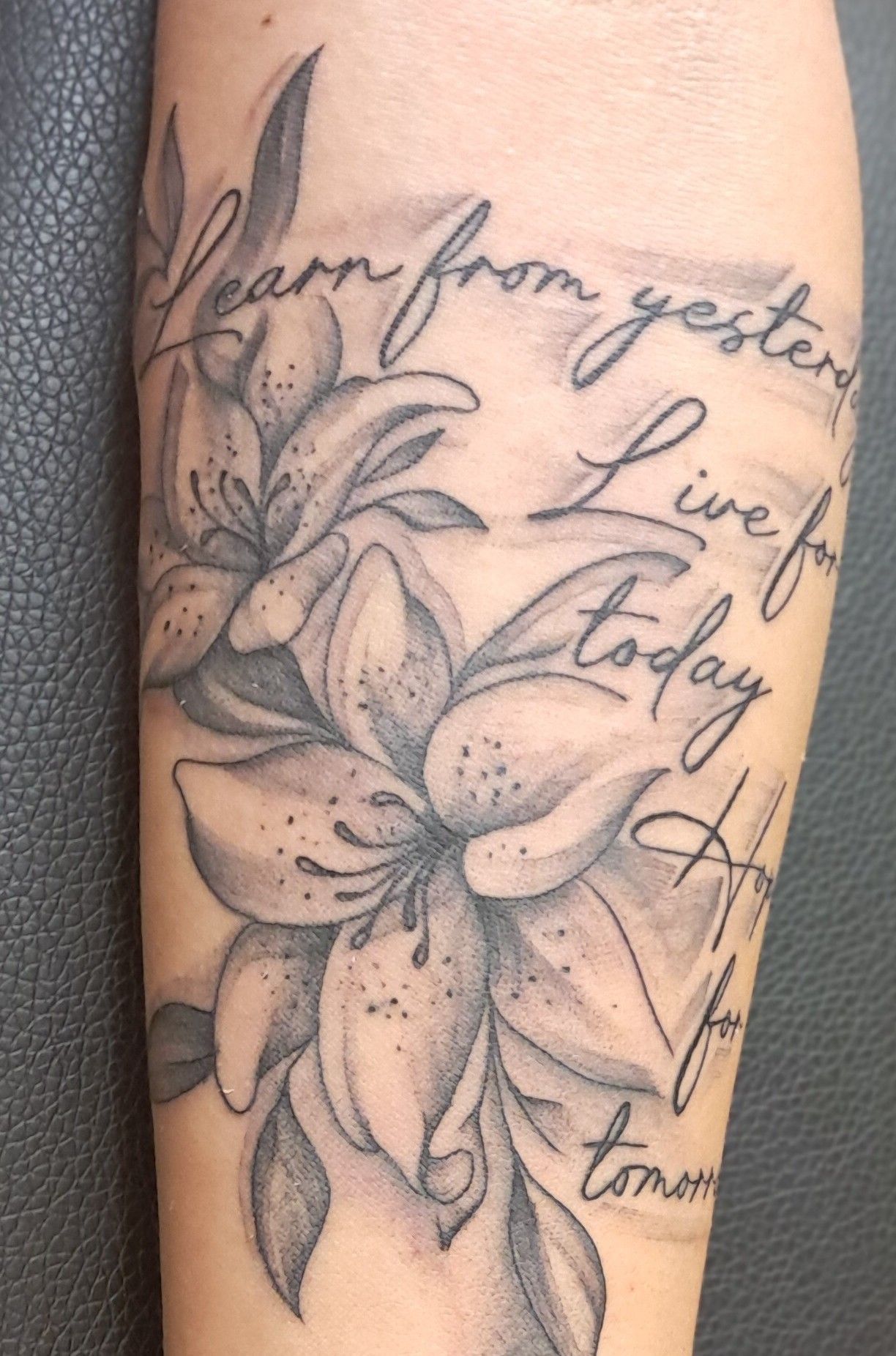 Tattoo of two lilies with leaves and cursive text: 