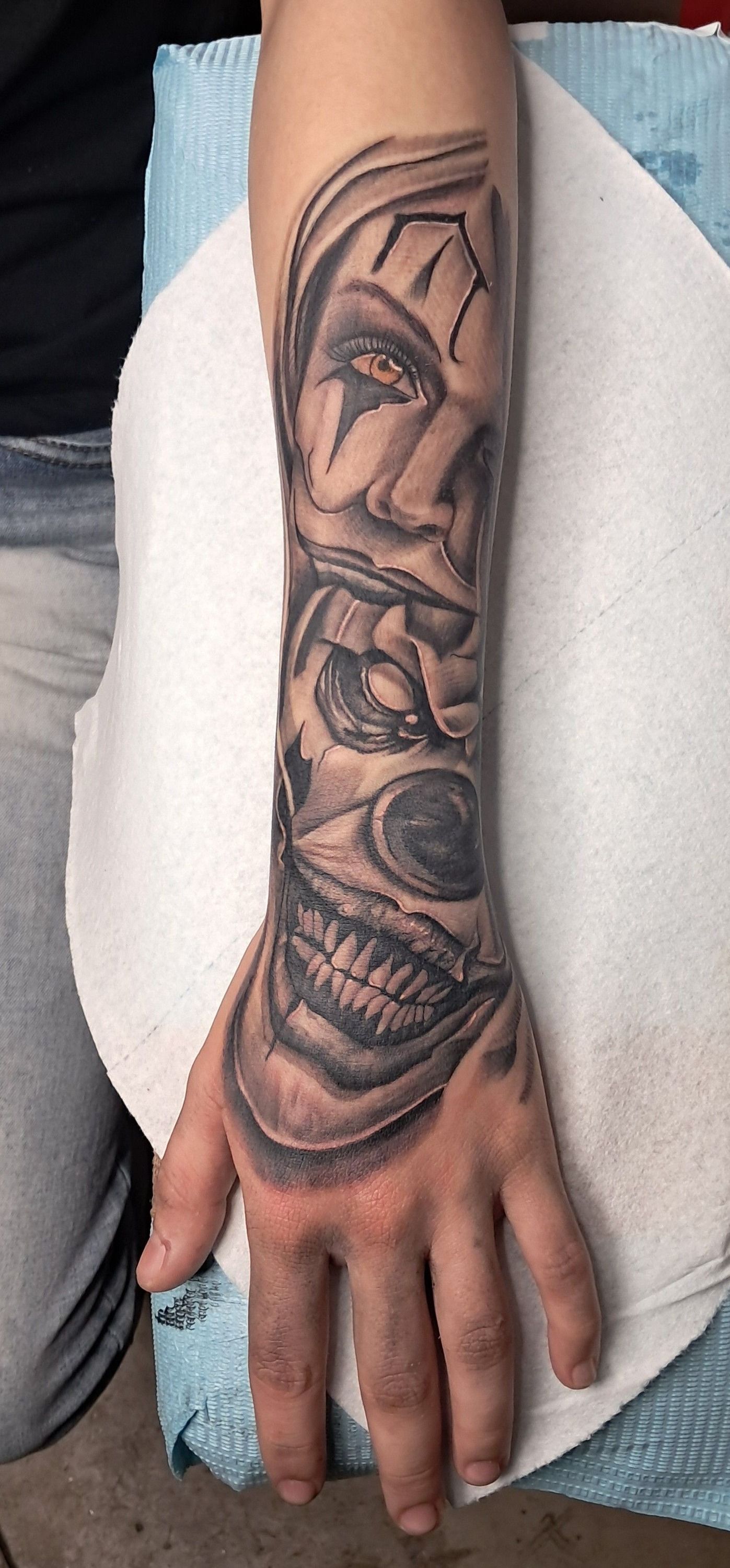 Tattoo of a creepy clown face on a forearm. The art is black and grey.