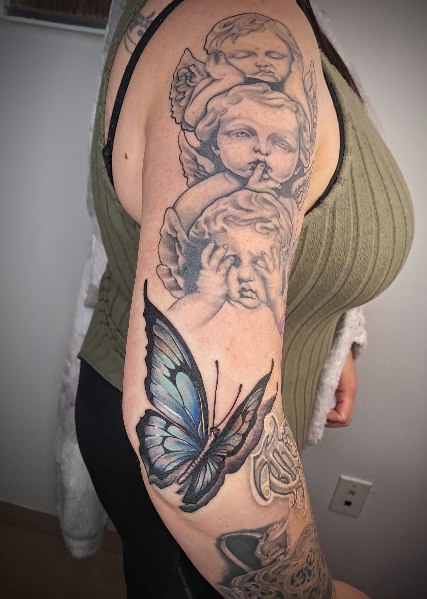 Person with arm tattoo featuring cherubs and a blue butterfly.