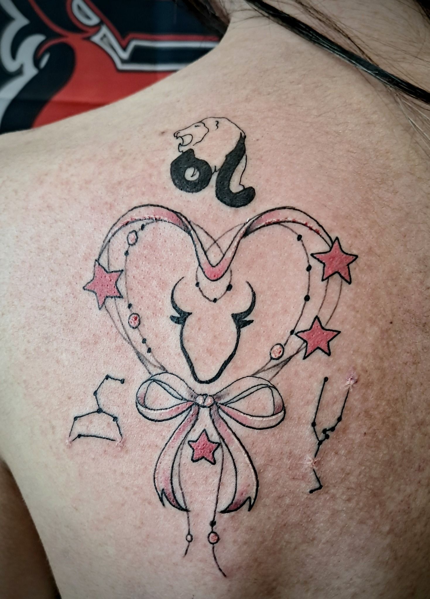 Tattoo of a heart-shaped design with a bull, ribbon, stars, and the Leo zodiac symbol on a person's back.