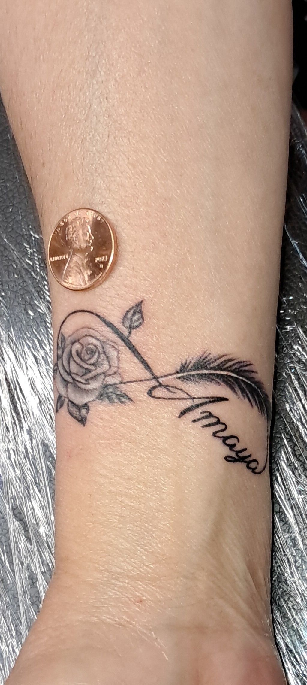Tattoo of a rose, feather, and infinity symbol with the name 