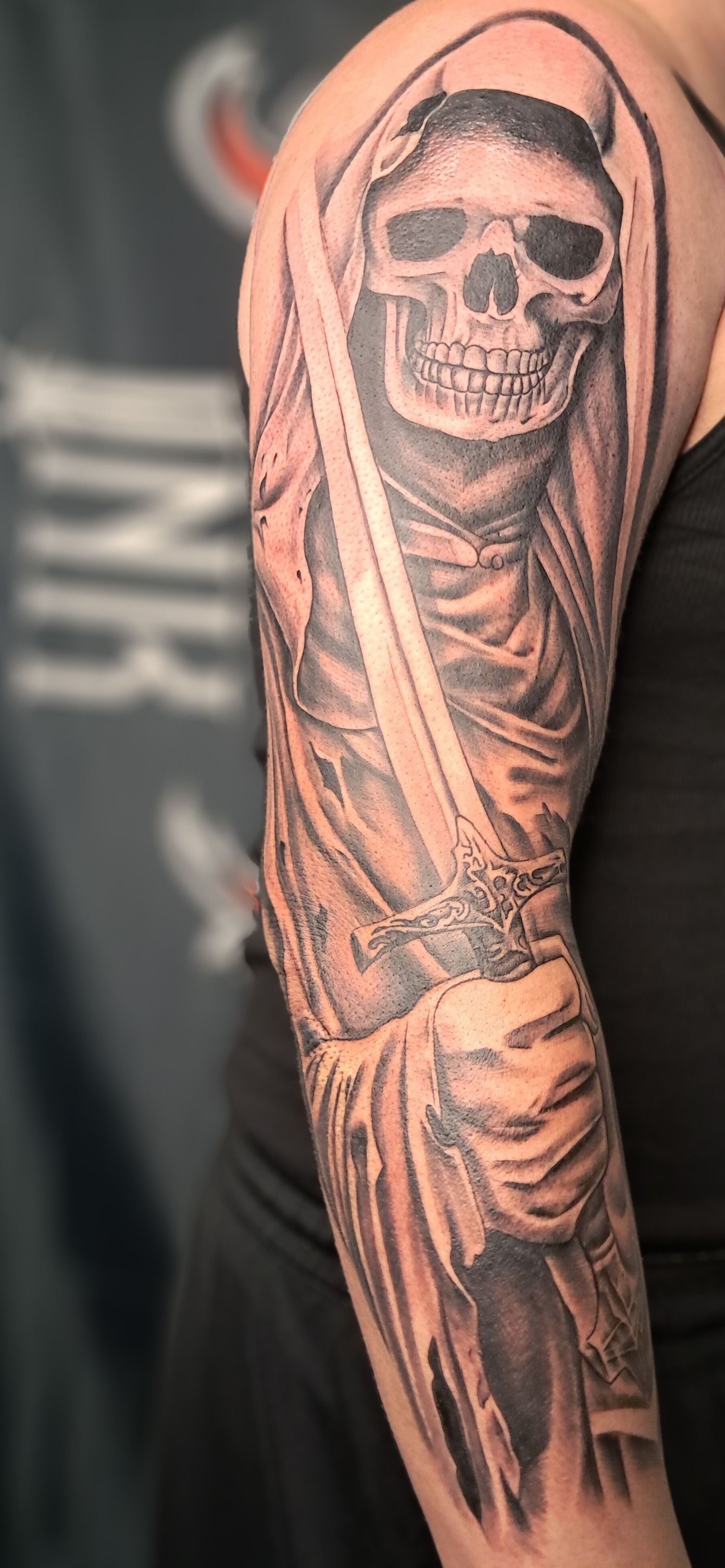 Tattoo of a grim reaper holding a sword on a person's arm, in grayscale.