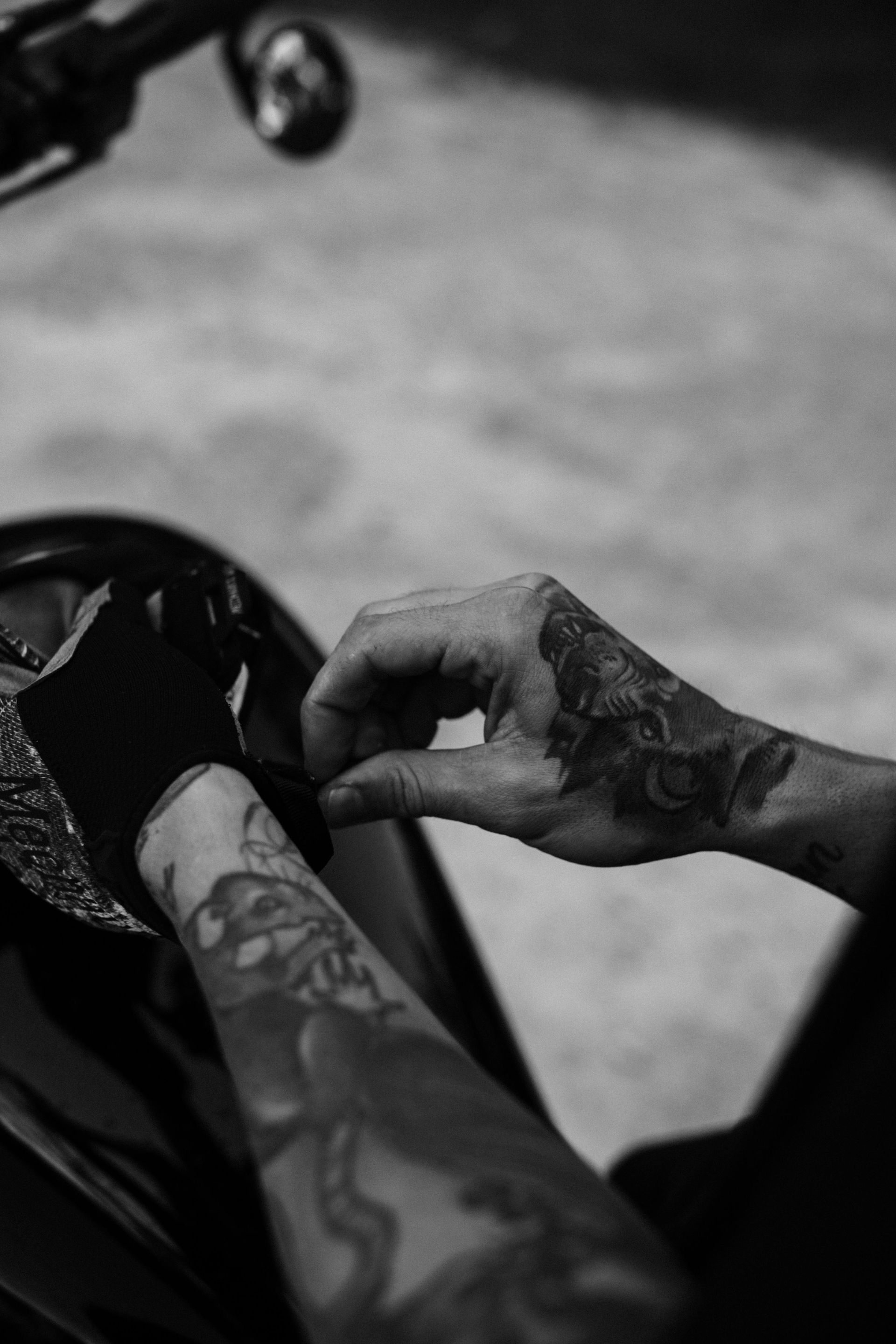 Person with tattooed arms adjusting black gloves on a motorcycle.