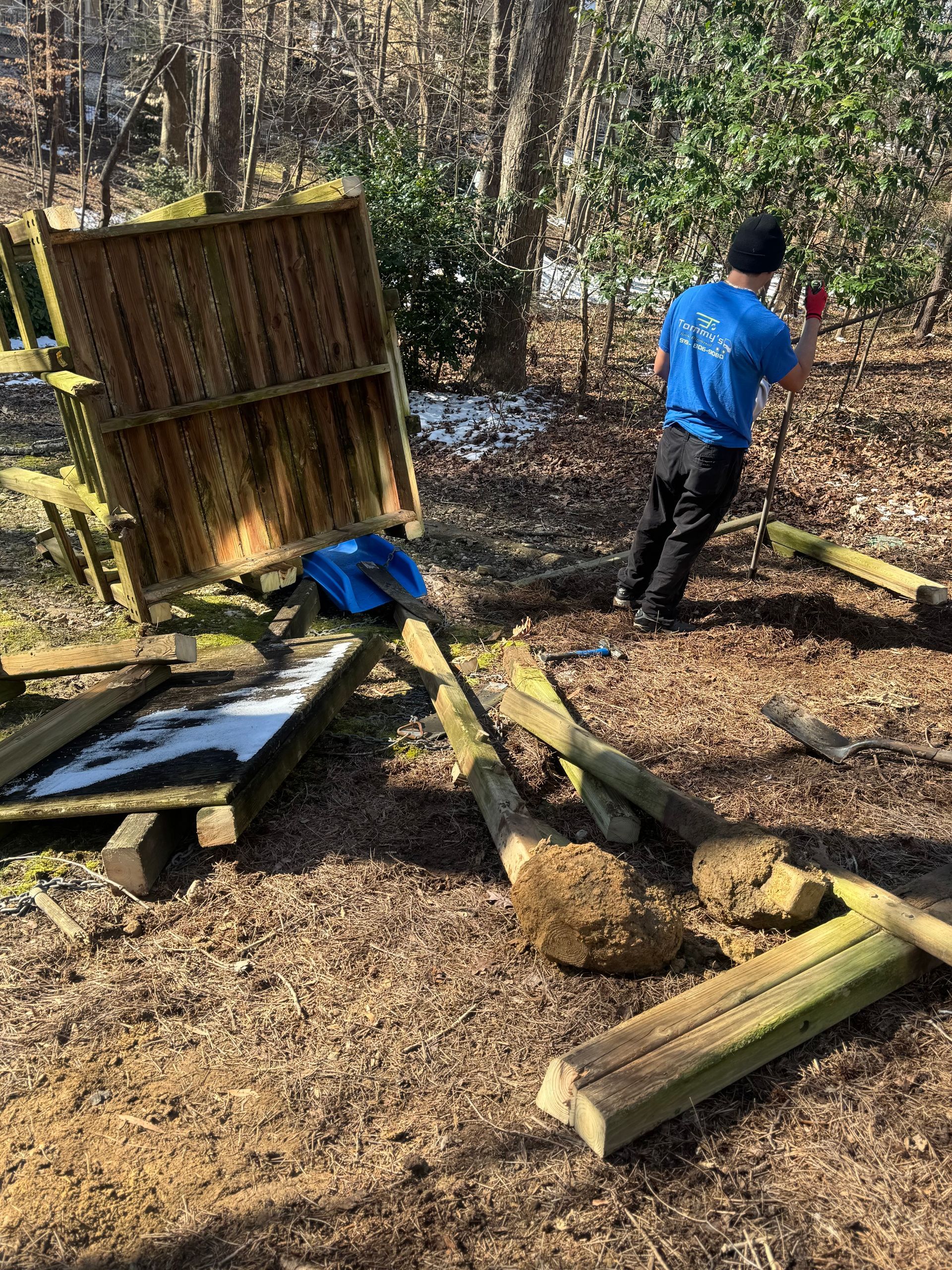 Man in blue shirt works on broken wooden structure outdoors.