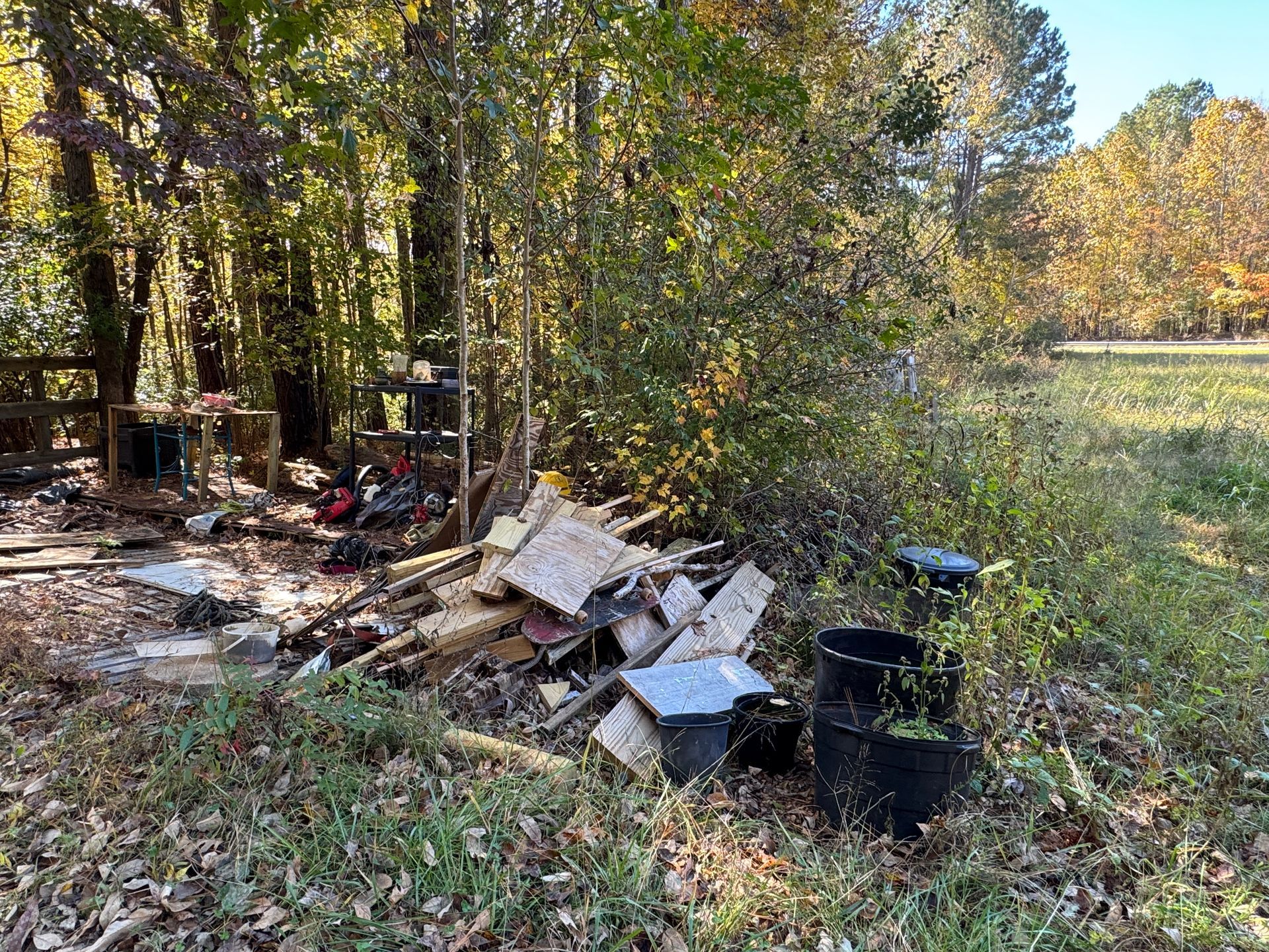 Pile of debris with black bins in a wooded area next to a grassy field.