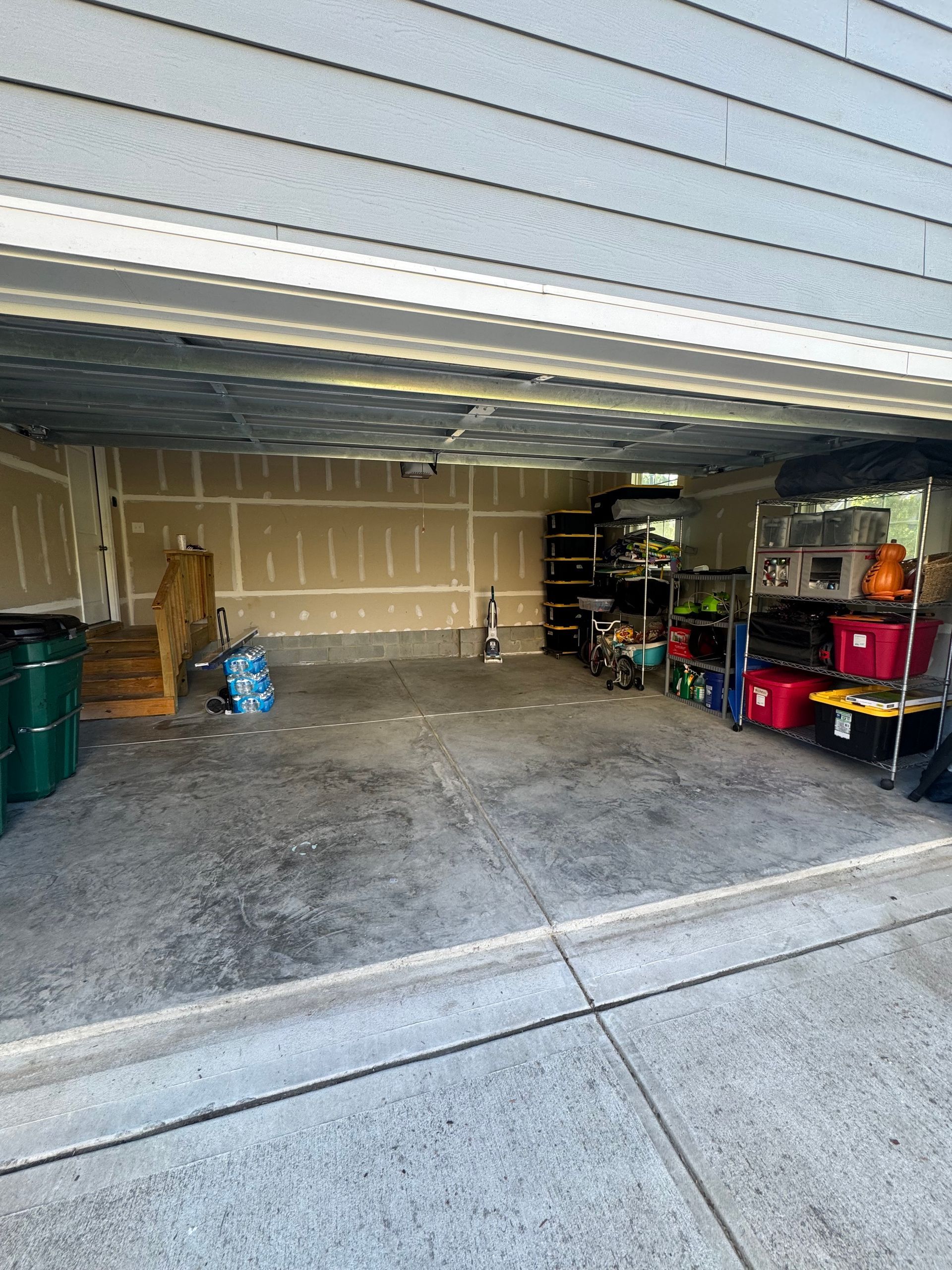 A partially filled garage with various items, including shelves and barrels, concrete floor, garage door open.
