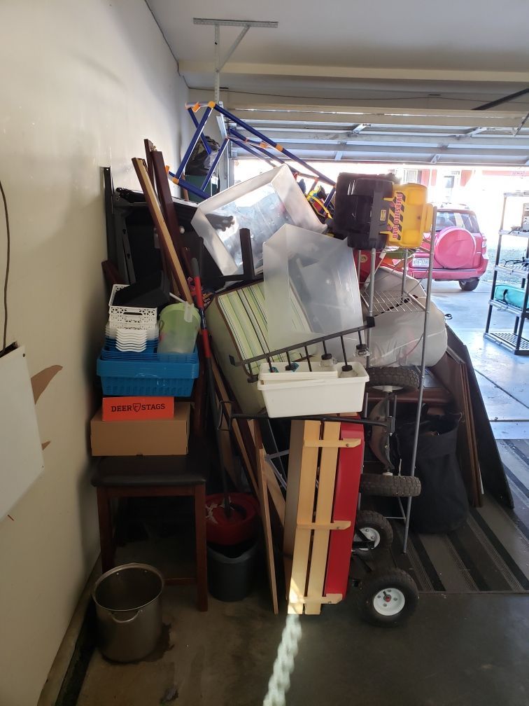 Cluttered garage: piles of boxes, tools, and household items. A red car is visible in the background.