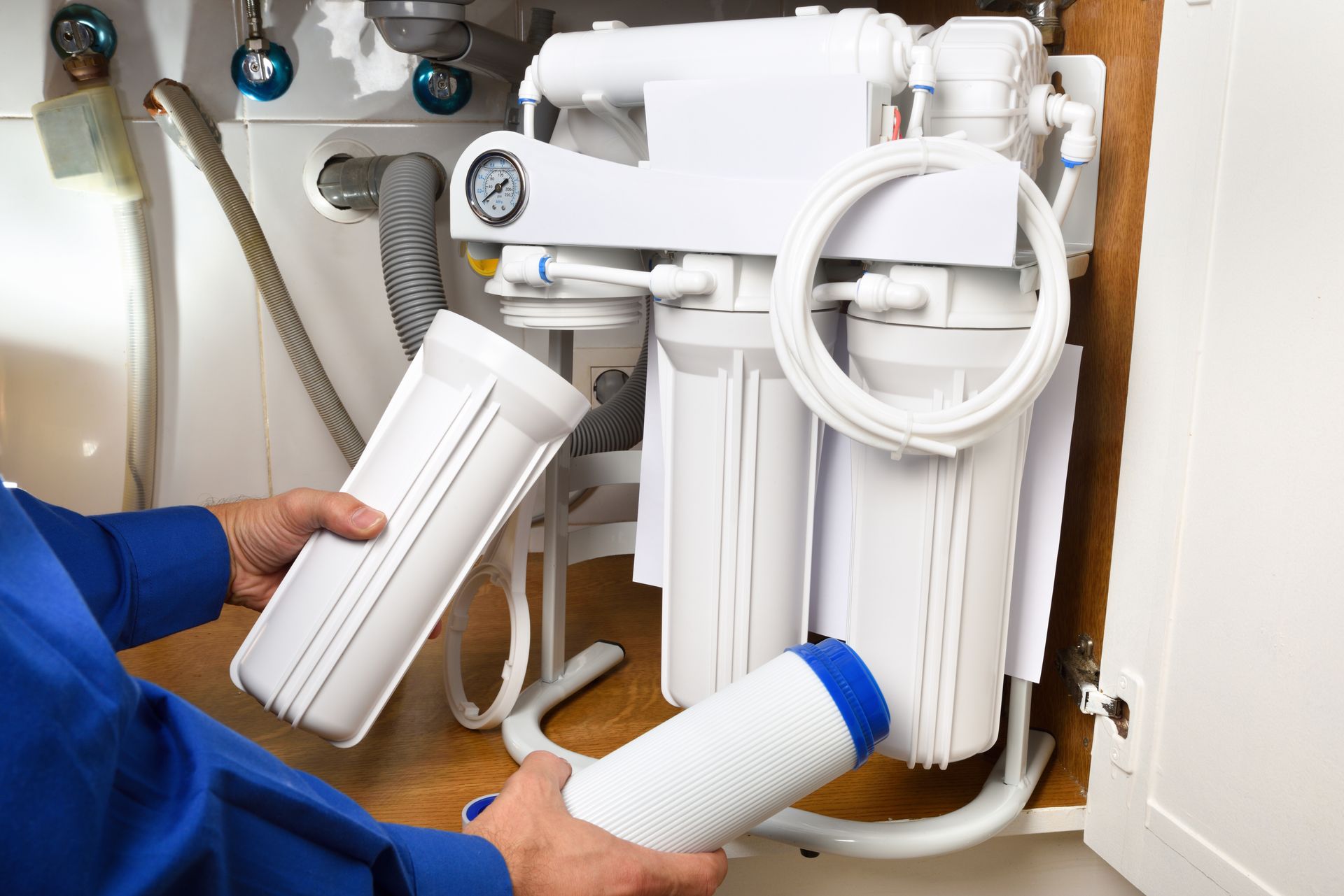 A man is fixing a water filter under a sink.