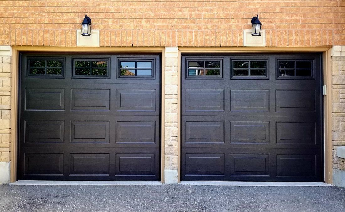 Deux portes de garage sombres avec fenêtres, flanquées de briques et de lumières.