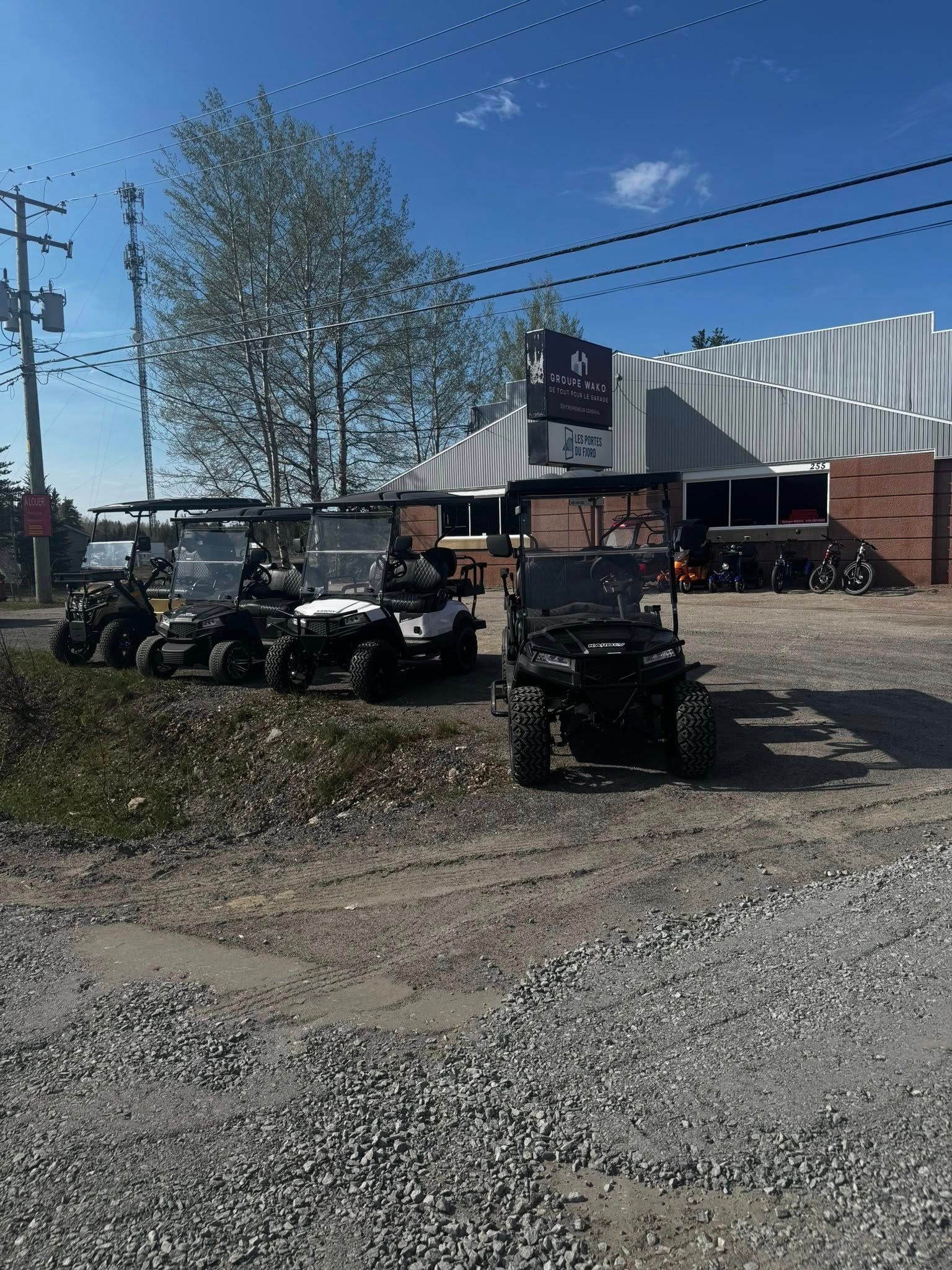 Voiturettes de golf garées sur du gravier devant un bâtiment. Ciel bleu clair.