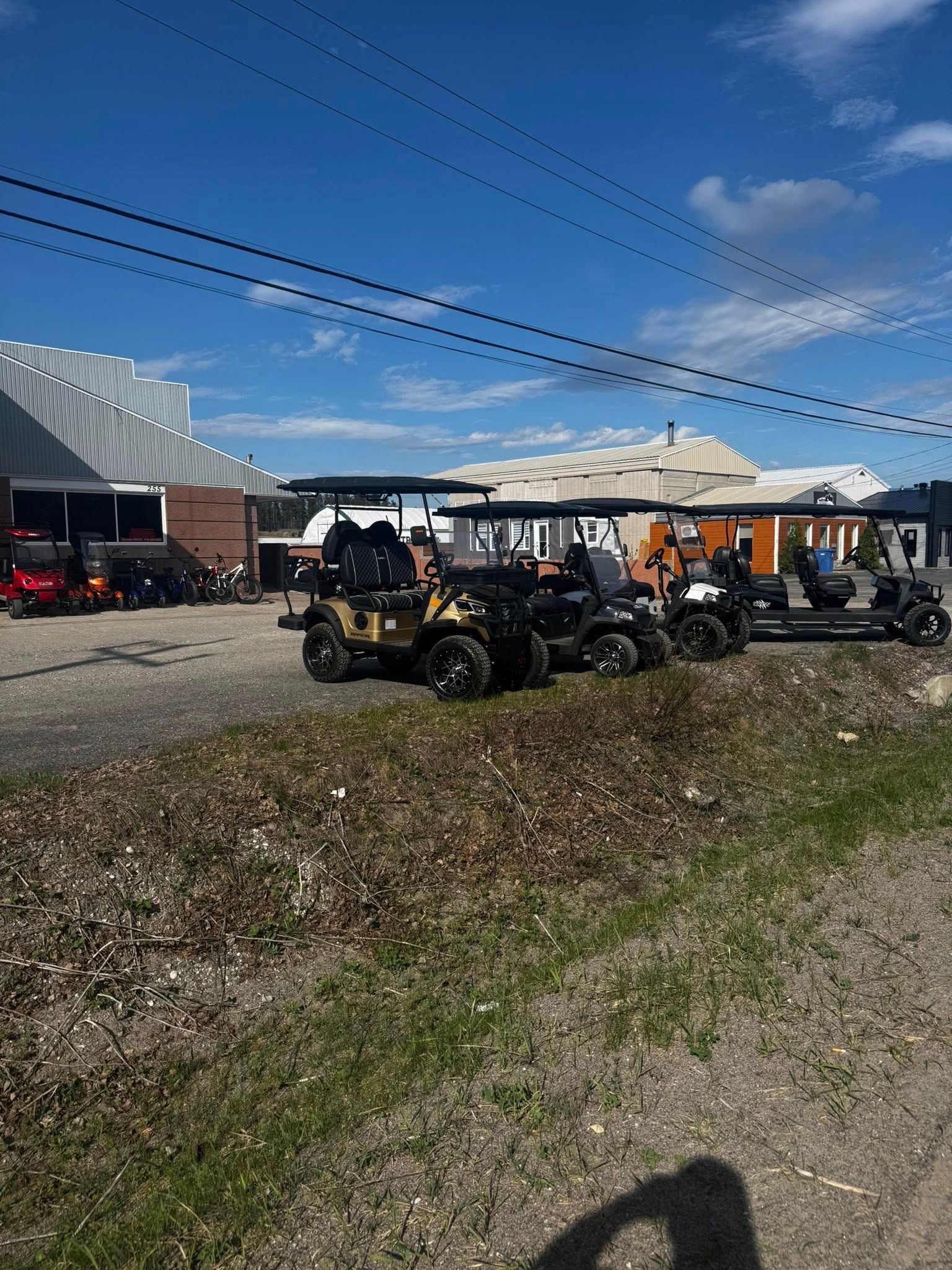 Plusieurs véhicules tout-terrain stationnés dans un terrain devant un bâtiment, sous un ciel bleu.