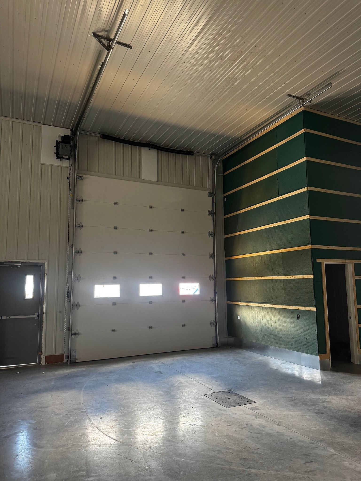 Vue intérieure d'un garage avec une porte basculante blanche fermée, des sols gris et un mur vert.