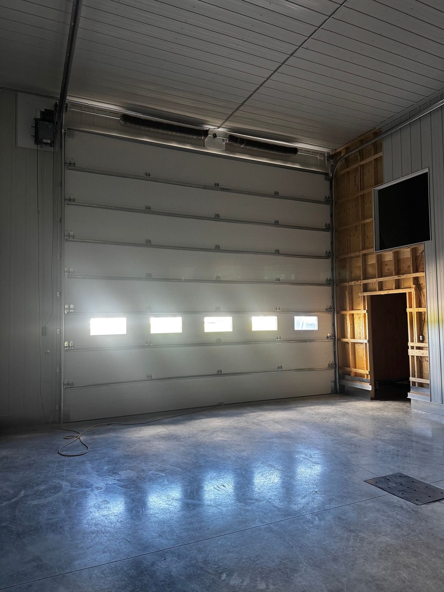 Intérieur d'un garage avec une grande porte fermée. La lumière du soleil entre par les fenêtres.