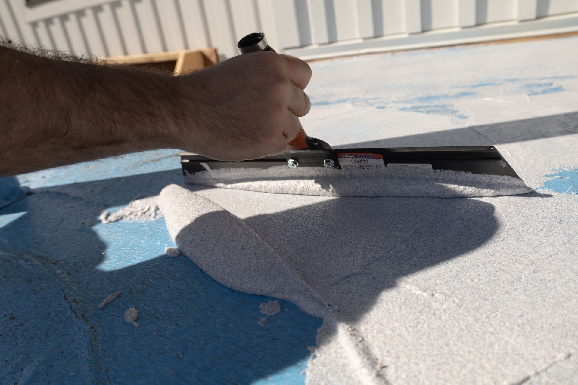 Personne utilisant une truelle pour étaler du stuc blanc sur une surface bleue. Extérieur, ensoleillé.