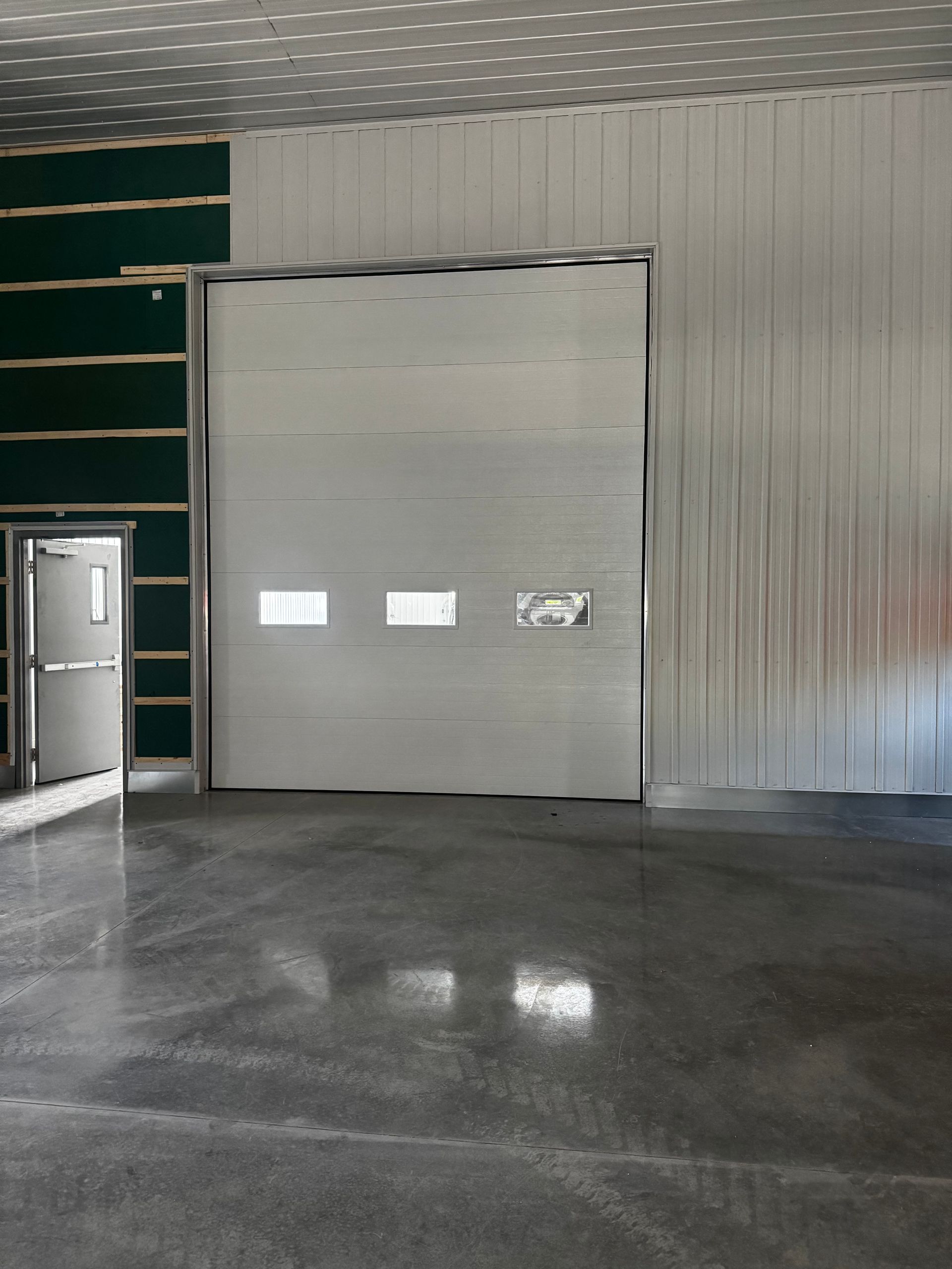 Intérieur d'entrepôt vide avec une porte de garage fermée et une porte latérale ouverte.