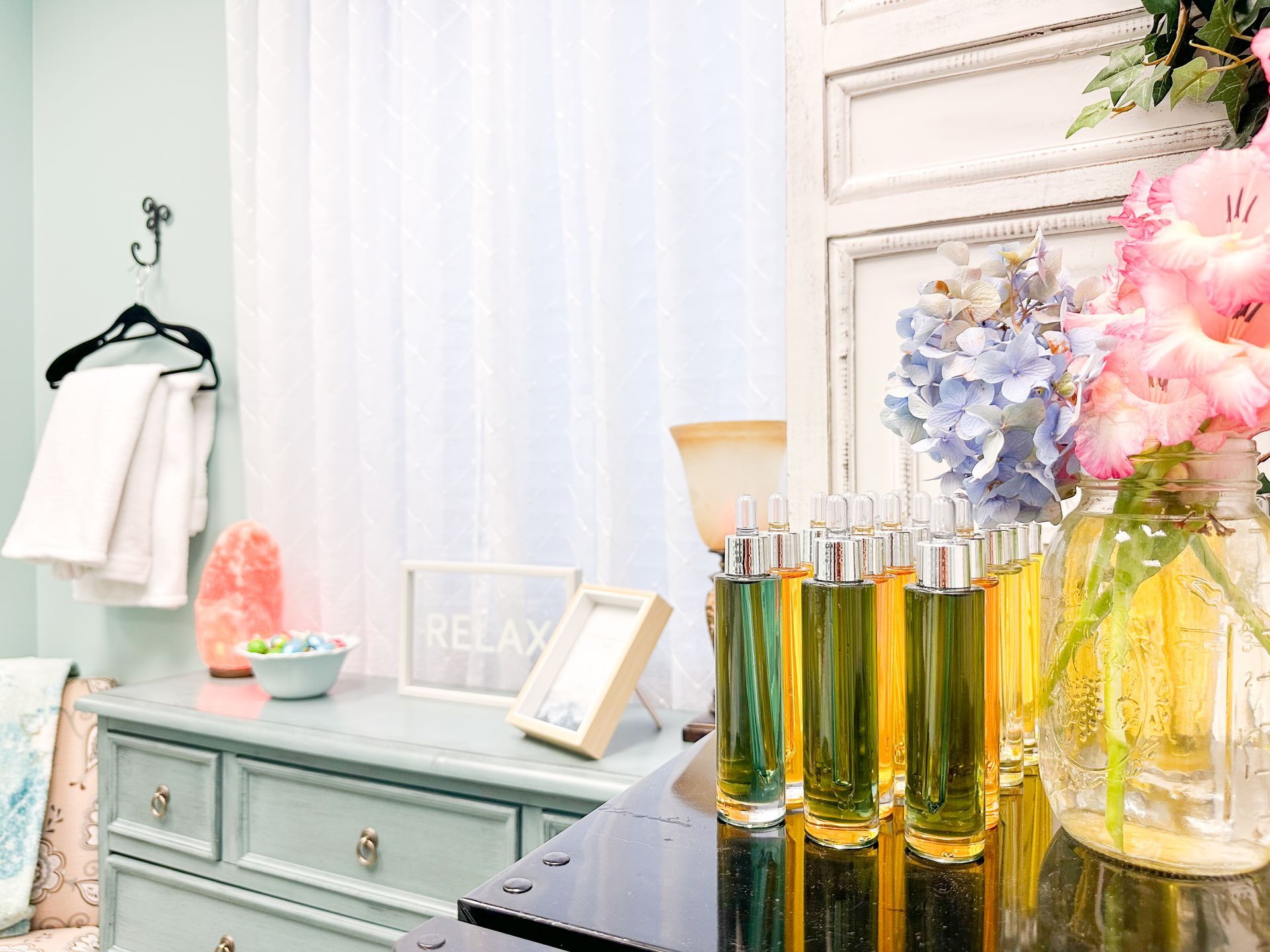 A bathroom with a dresser , vase of flowers and bottles of perfume.