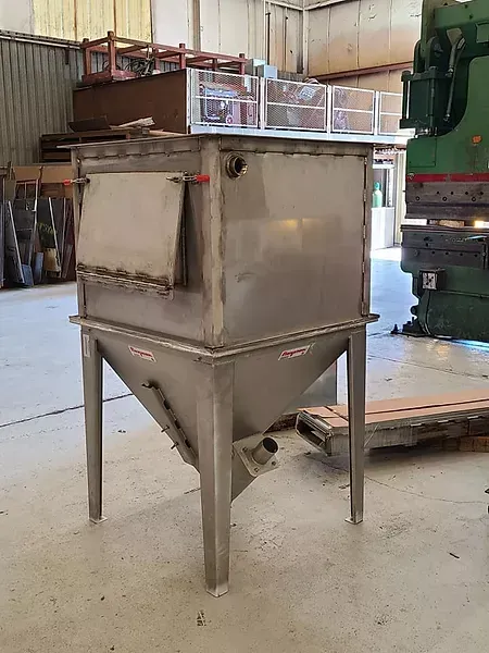 A stainless steel tank is sitting in a warehouse next to a green machine.