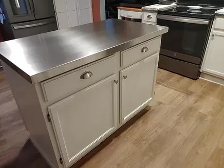 A kitchen island with a stainless steel top and white cabinets.