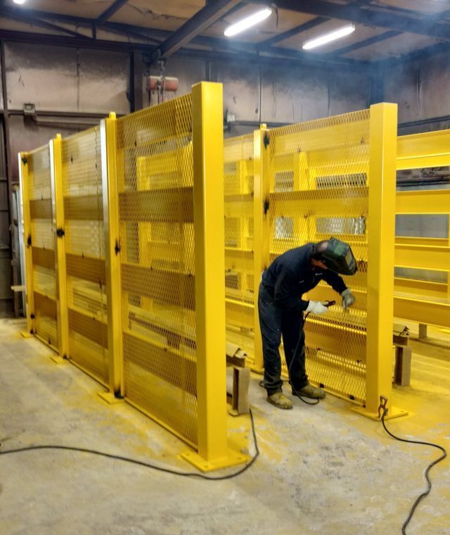 A man is working on a yellow fence in a factory.