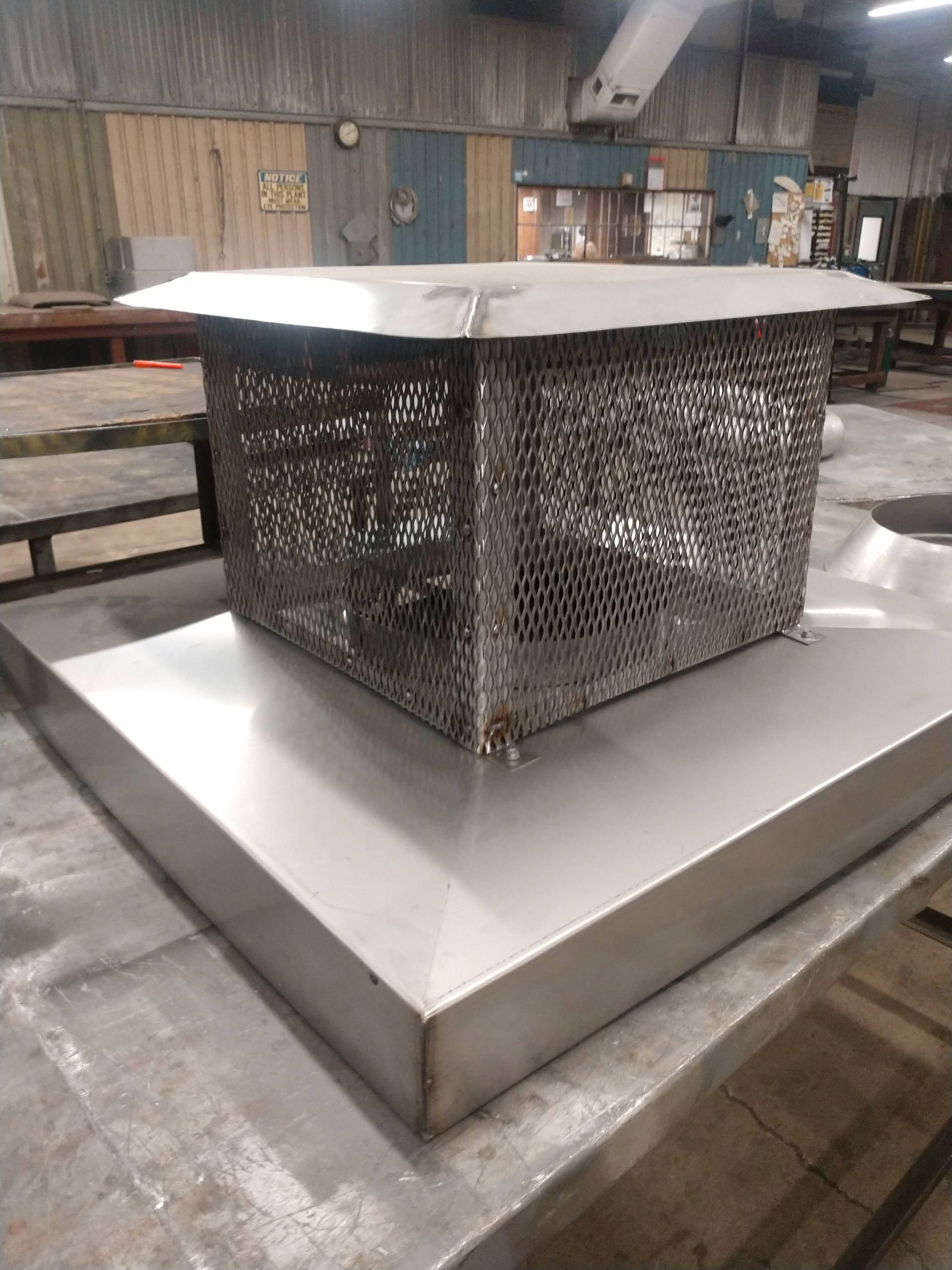 A stainless steel chimney cap is sitting on top of a metal table.