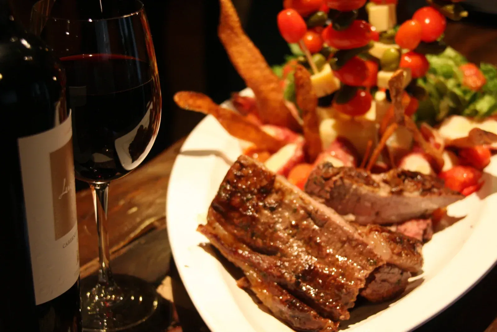 Un plato de comida junto a una copa de vino y una botella de vino.