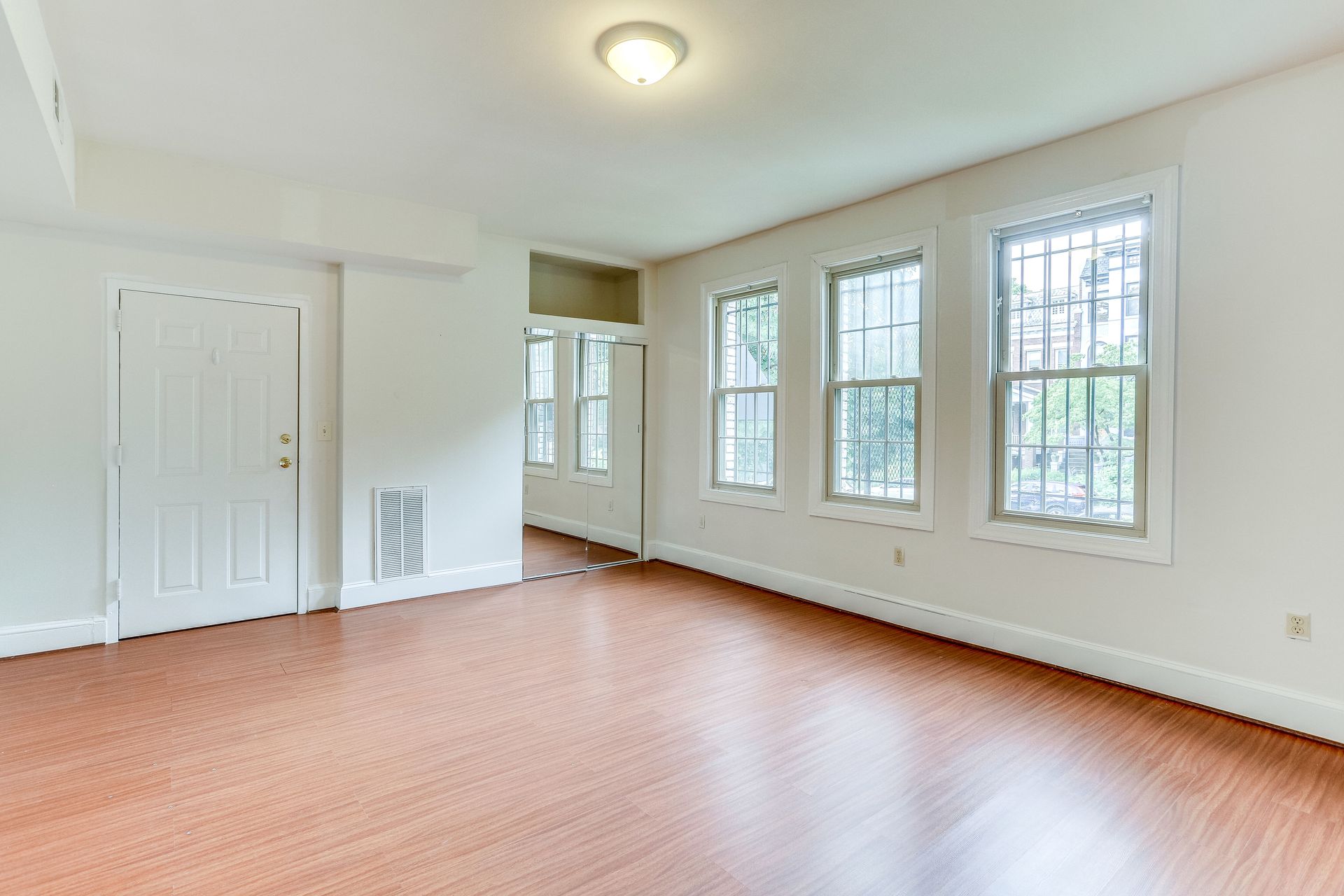 An empty living room with hardwood floors and a large mirror.