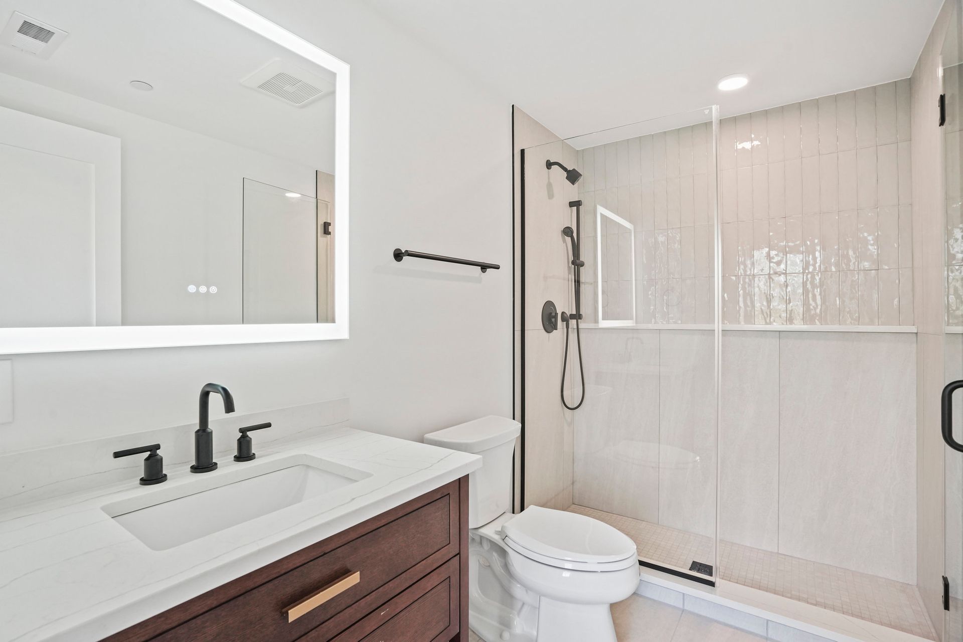 A bathroom with a toilet , sink , mirror and walk in shower.