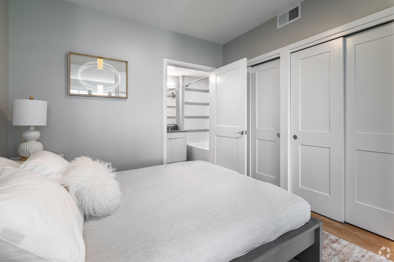 A bedroom with a bed , closet , lamp and mirror.