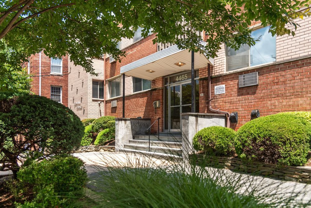 A brick building with a porch and stairs surrounded by bushes and trees.