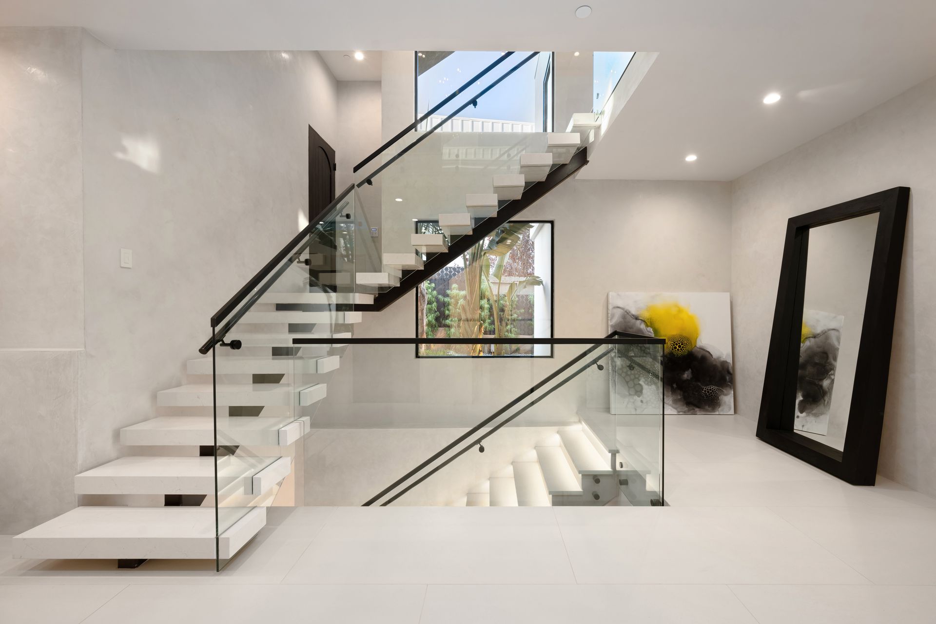Modern staircase with glass railing and floating steps in a bright white interior.