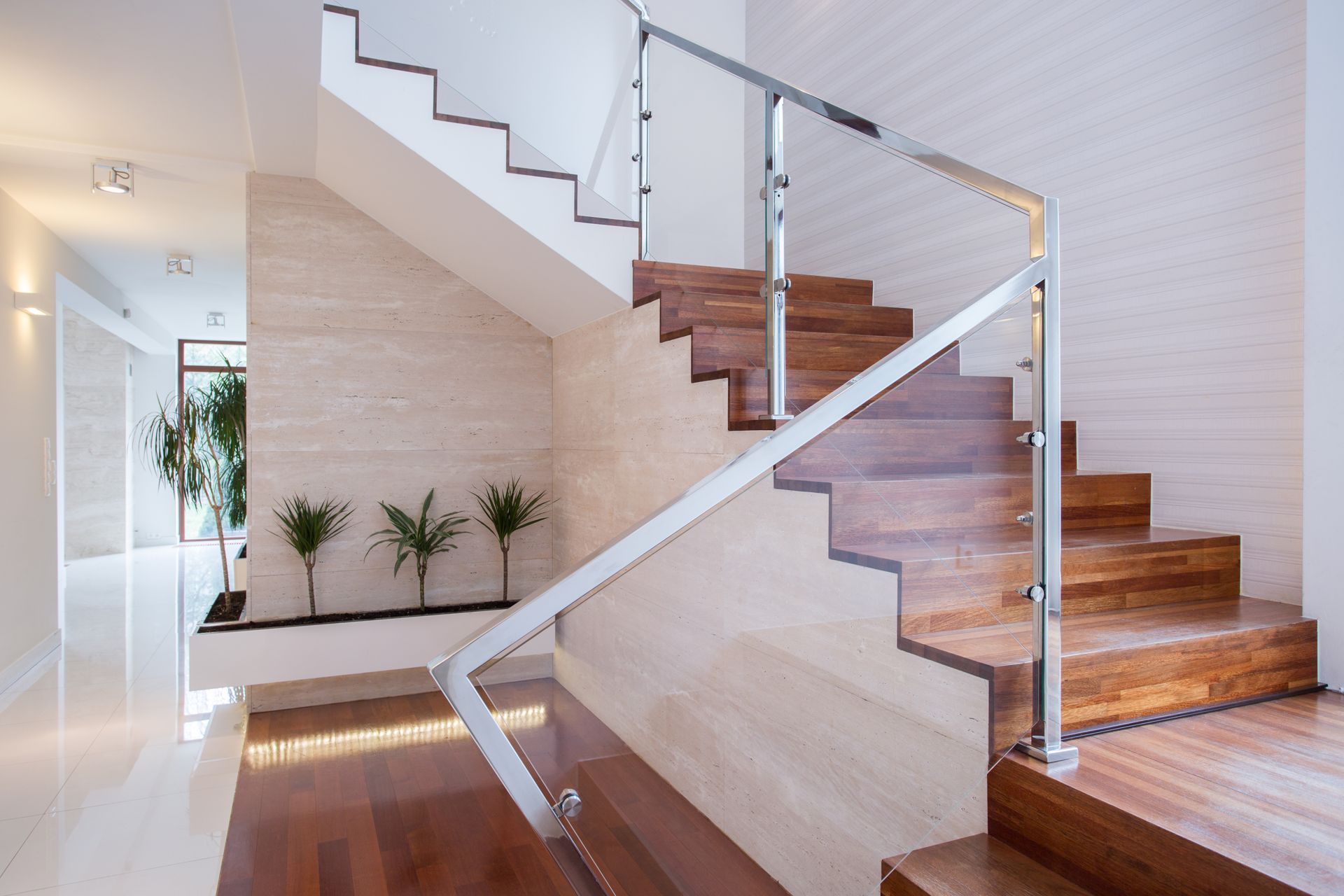 Wooden staircase with glass railing and beige stone wall, lit interior.