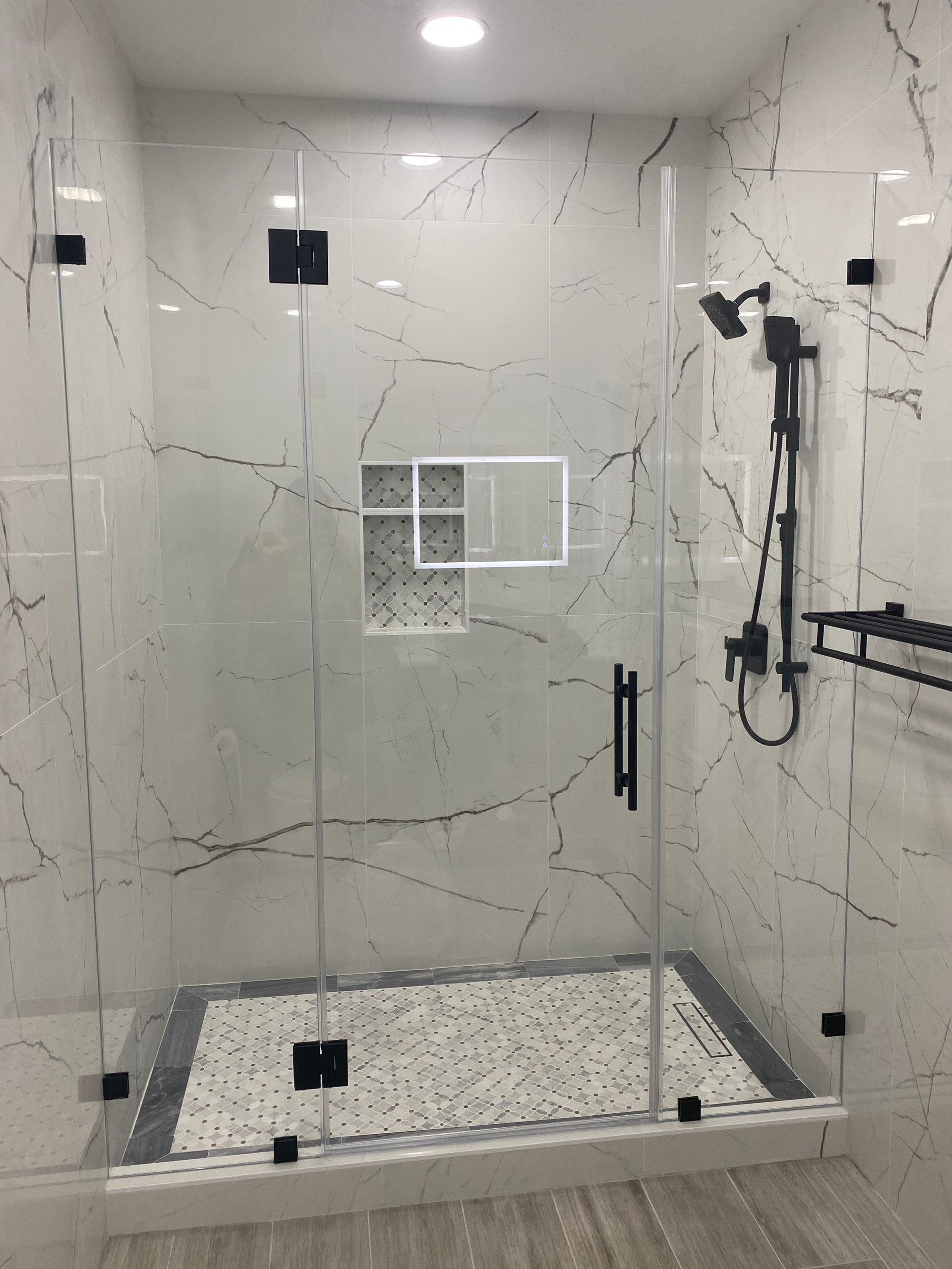 Modern shower with glass doors, black fixtures, and marble-like tile.
