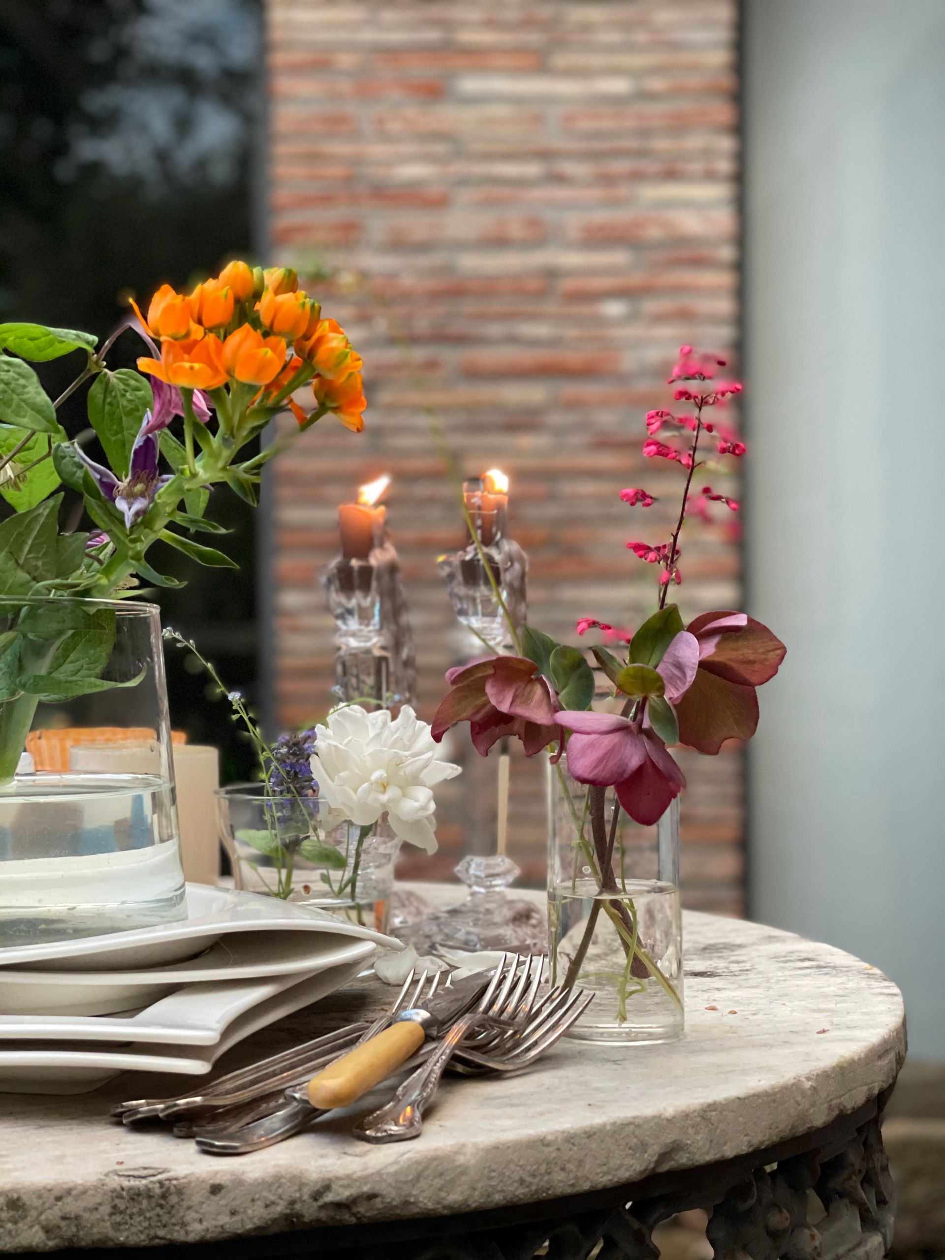 Apparecchiatura della tavola con fiori, candele e posate su un tavolo di pietra all'esterno.