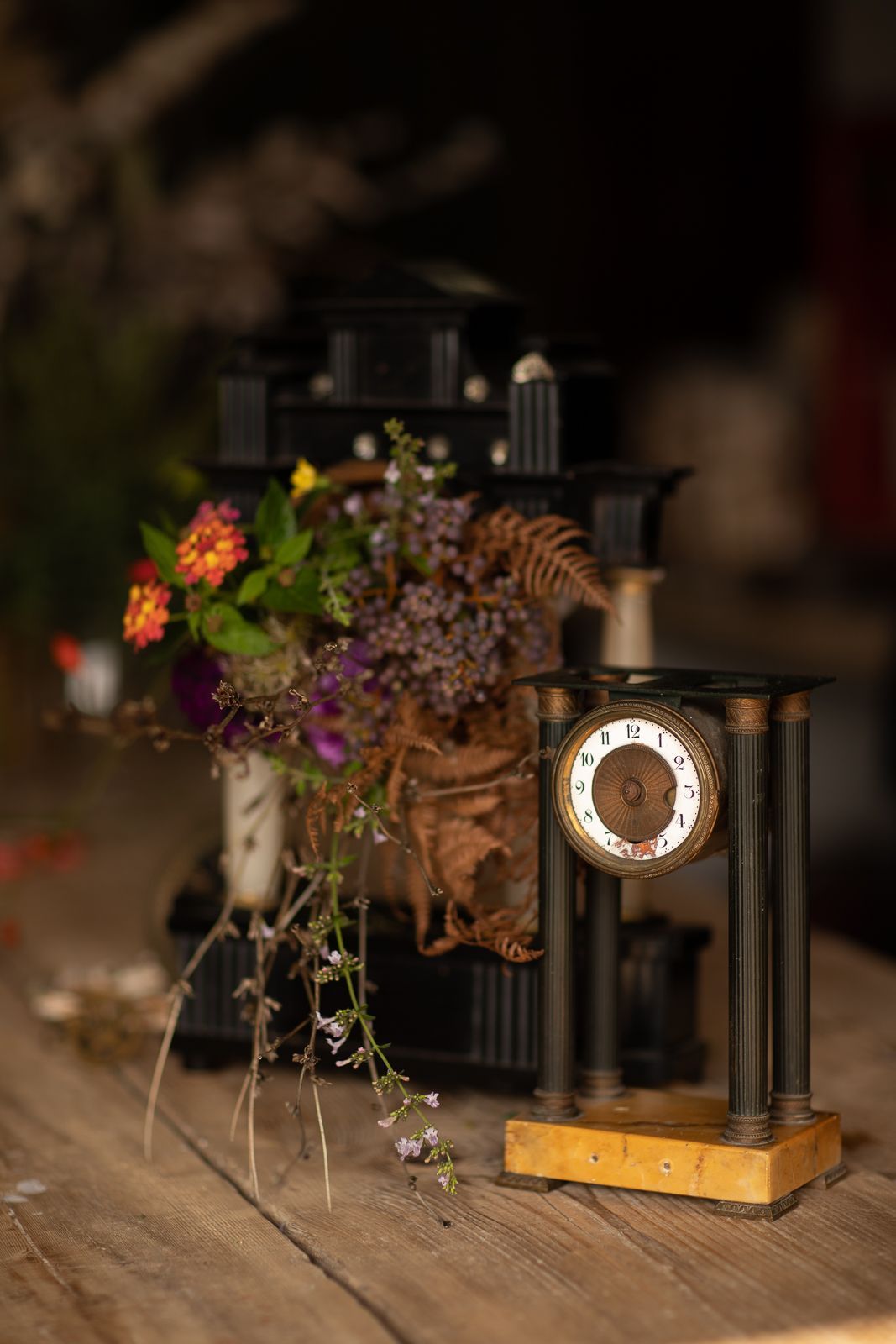 Orologio antico con pilastri neri e base dorata, vicino a un mazzo di fiori.