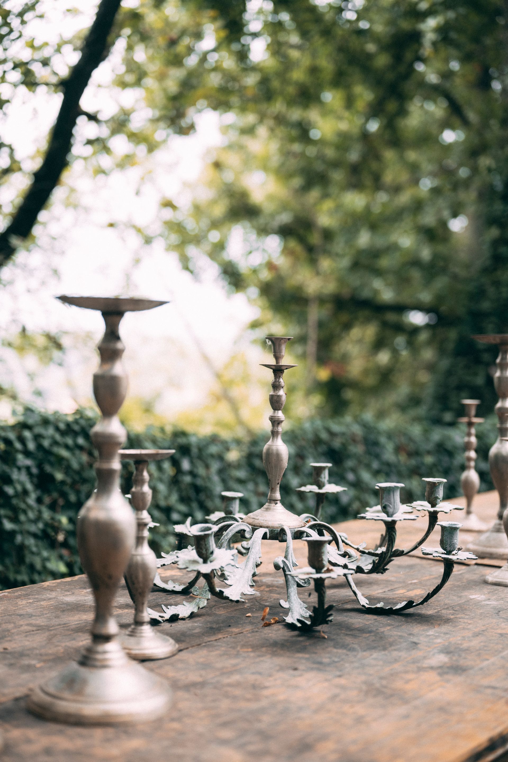 Portacandele di varie dimensioni su un tavolo di legno all'aperto con uno sfondo verde sfocato.