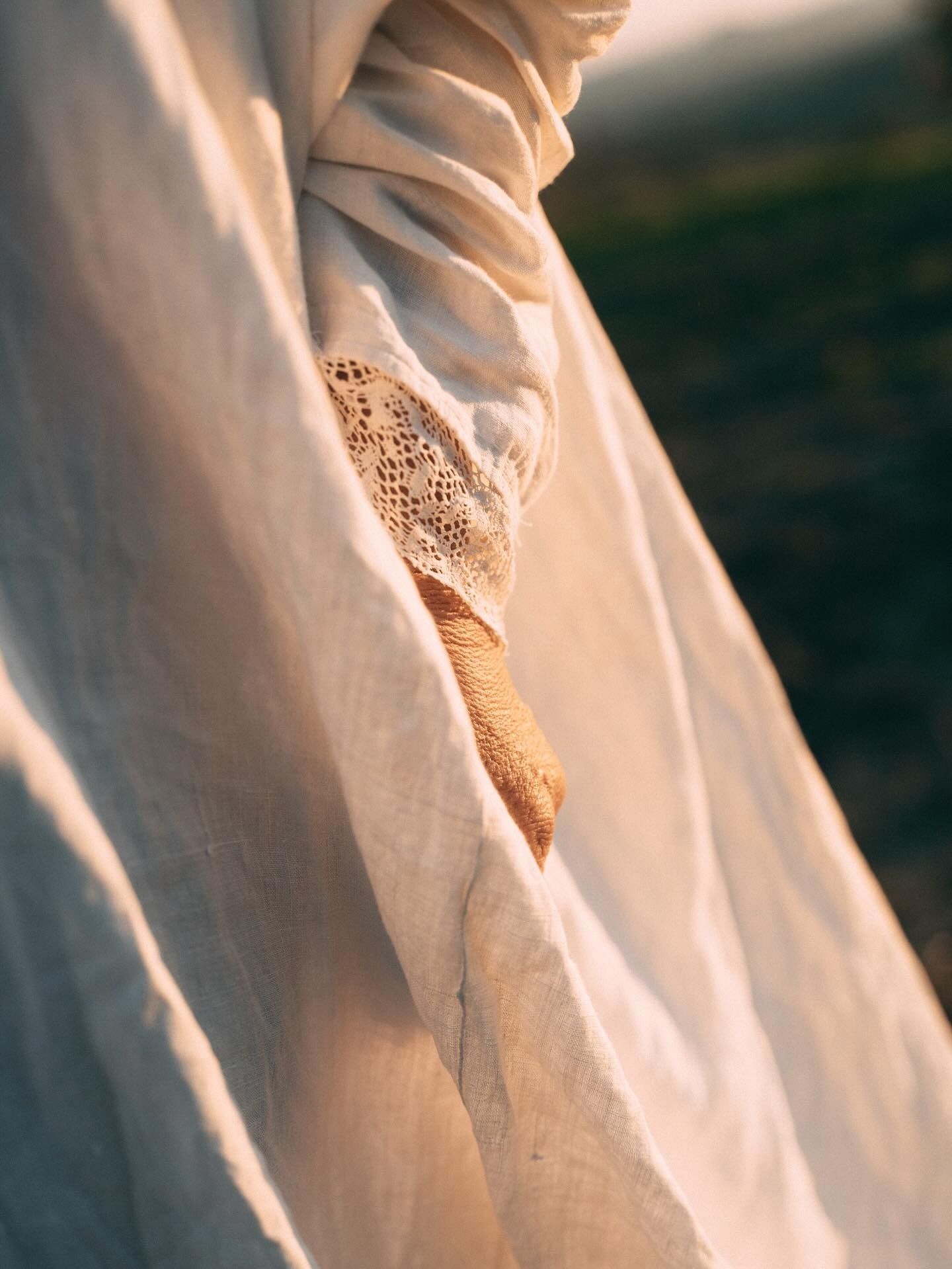 Braccio drappeggiato in tessuto color crema, manica in pizzo dettagliato, texture che mette in risalto la luce del sole.