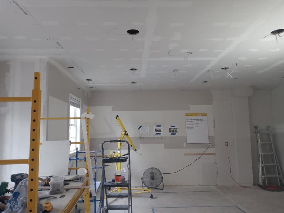 Interior under construction, drywall installed on walls and ceiling, with scaffolding and tools.
