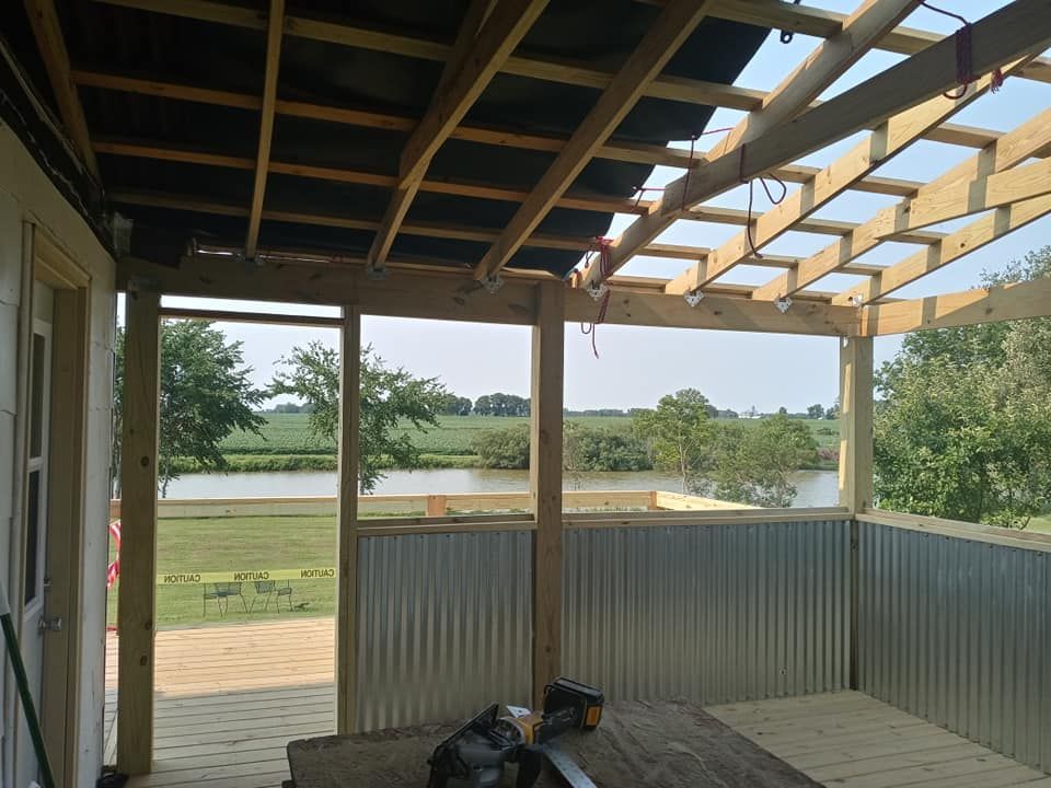 Wooden deck with corrugated metal walls overlooking a river and farmland.