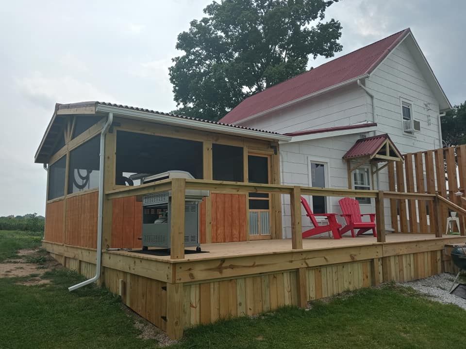 Wooden deck with screened-in porch attached to a white house with red roof. Two red chairs sit on the deck.