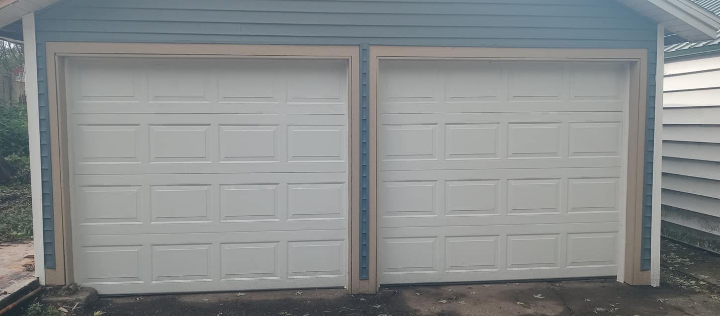 Two white garage doors on a blue-sided building with tan trim.